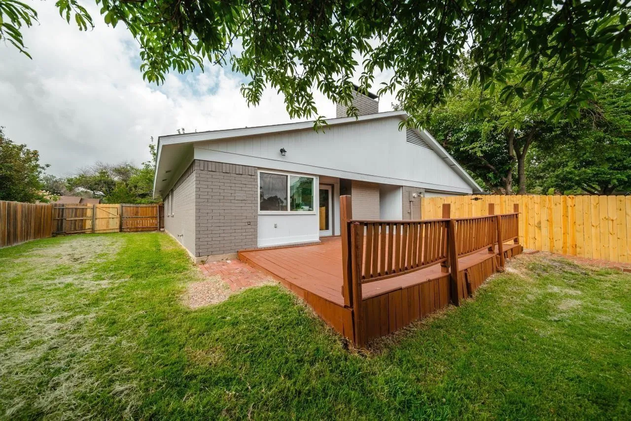 Exterior features including a gray brick facade, a wood-finish raised deck, and a wood privacy fence surrounding a grass-covered backyard
