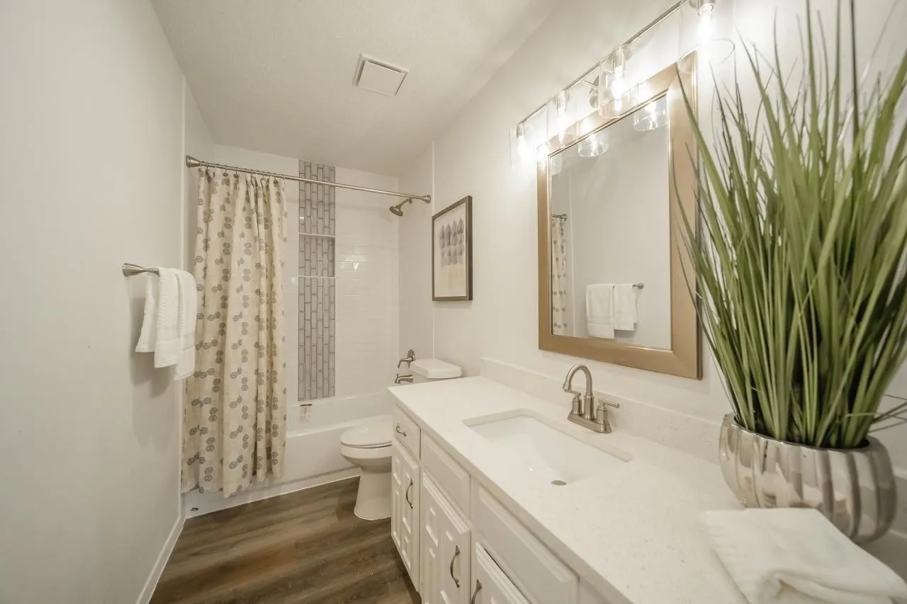 Bathroom featuring a white vanity with a quartz countertop, an integrated rectangular sink, wood-finish flooring, and a tub-shower combination with decorative vertical tile inlay