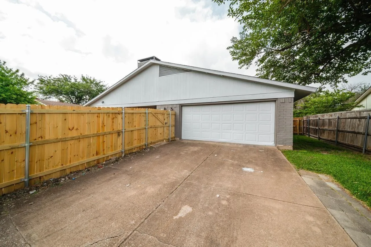 Attached two-car garage featuring a white sectional door, concrete driveway, and full wood privacy fencing