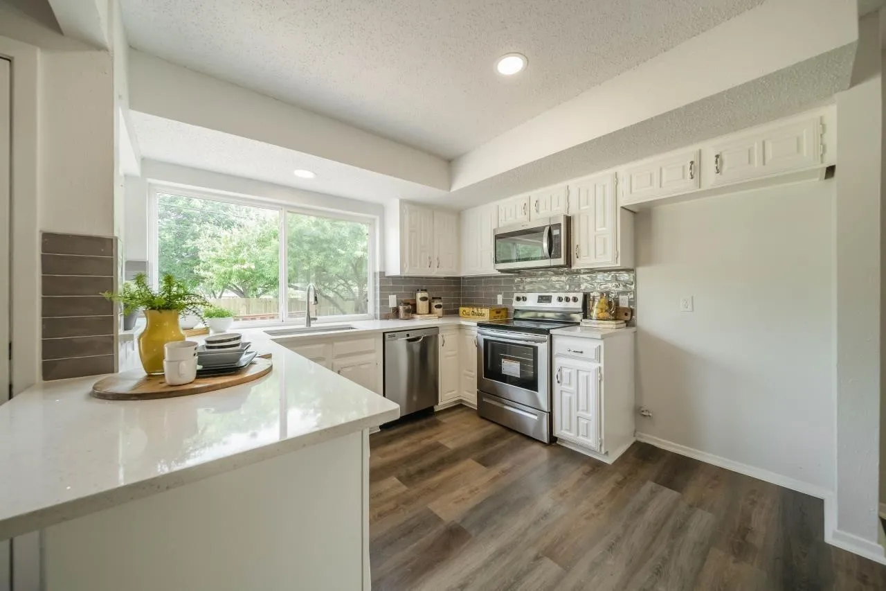 Kitchen featuring white cabinetry, stainless steel appliances, wood-finish flooring, quartz-style countertops, and a tile backsplash