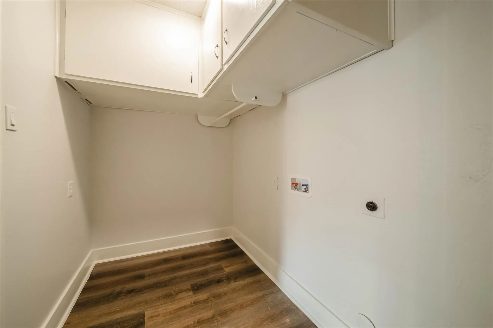 Utility area featuring wood-finish flooring, ceiling-mounted cabinetry, and dedicated plumbing connections