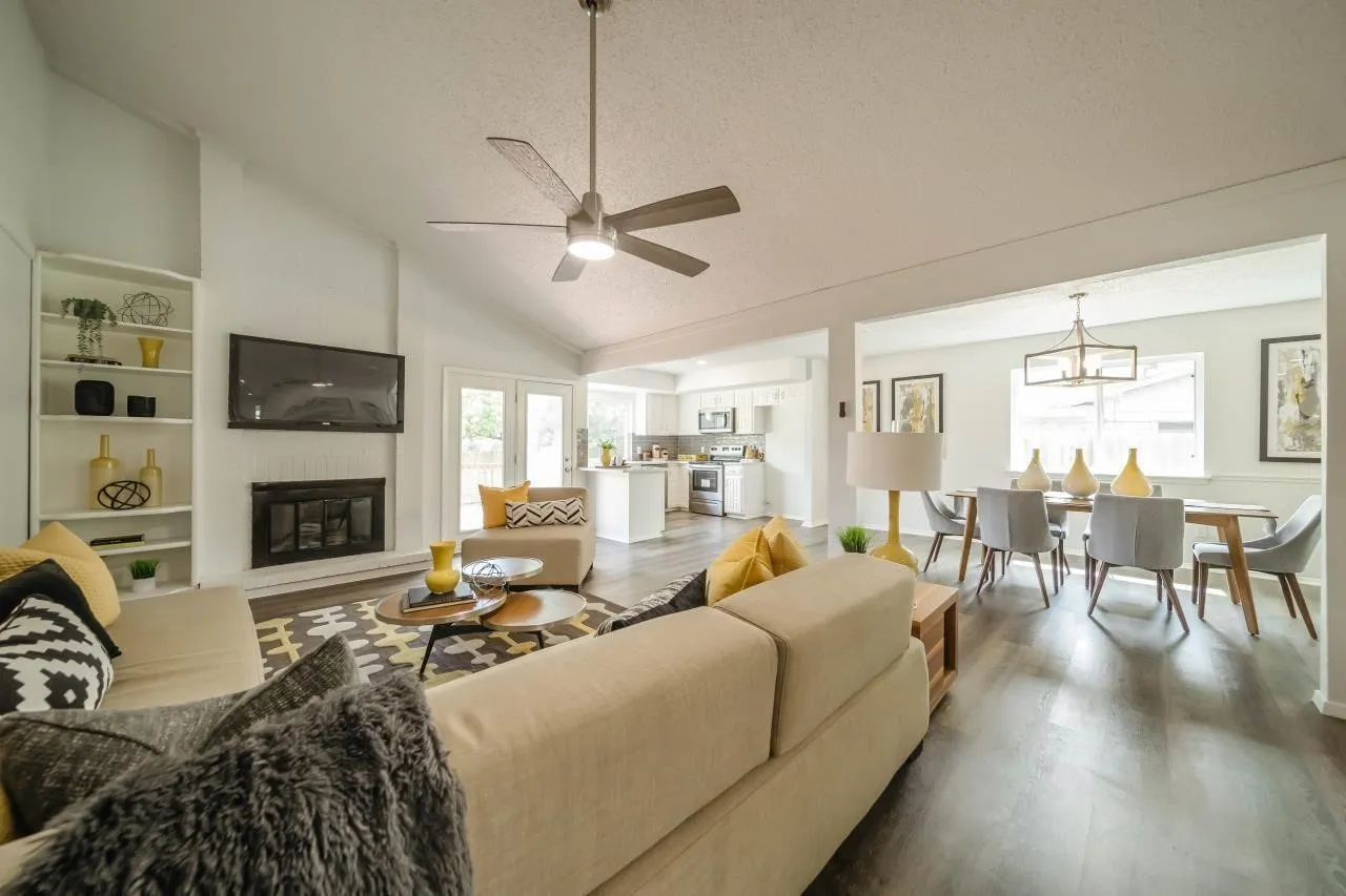 Vaulted ceiling with a central brushed-nickel ceiling fan, wood-finish flooring, built-in shelving, and a gas fireplace with a black surround