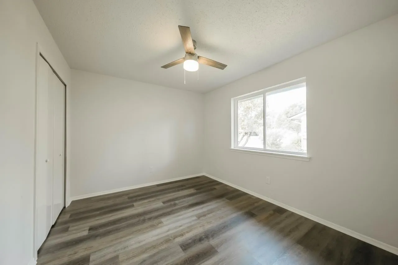 Neutral-toned interior featuring wood-finish flooring, sliding door closet, single-pane window, and integrated ceiling fan with lighting