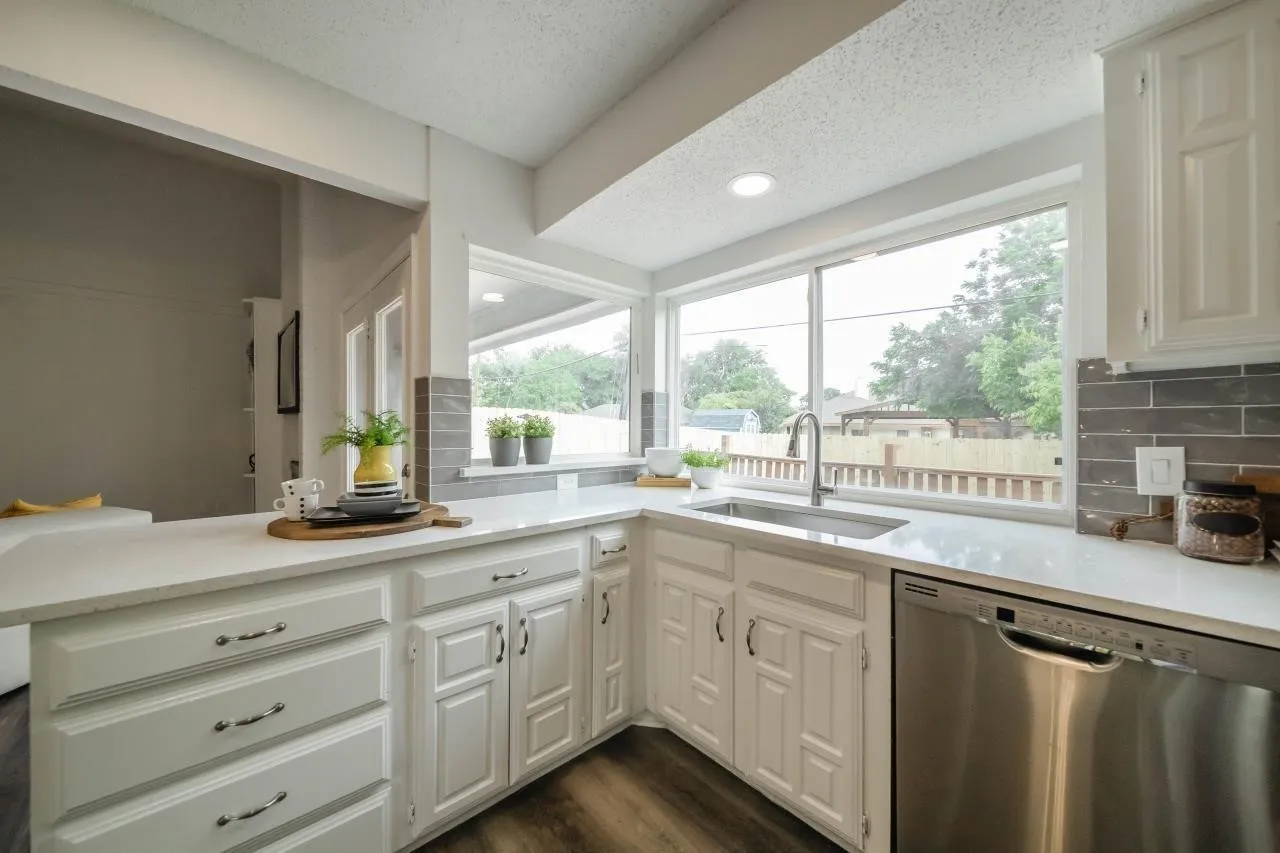 Kitchen featuring white cabinetry, quartz countertops, gray tile backsplash, stainless steel sink with high-arc faucet, and stainless steel dishwasher