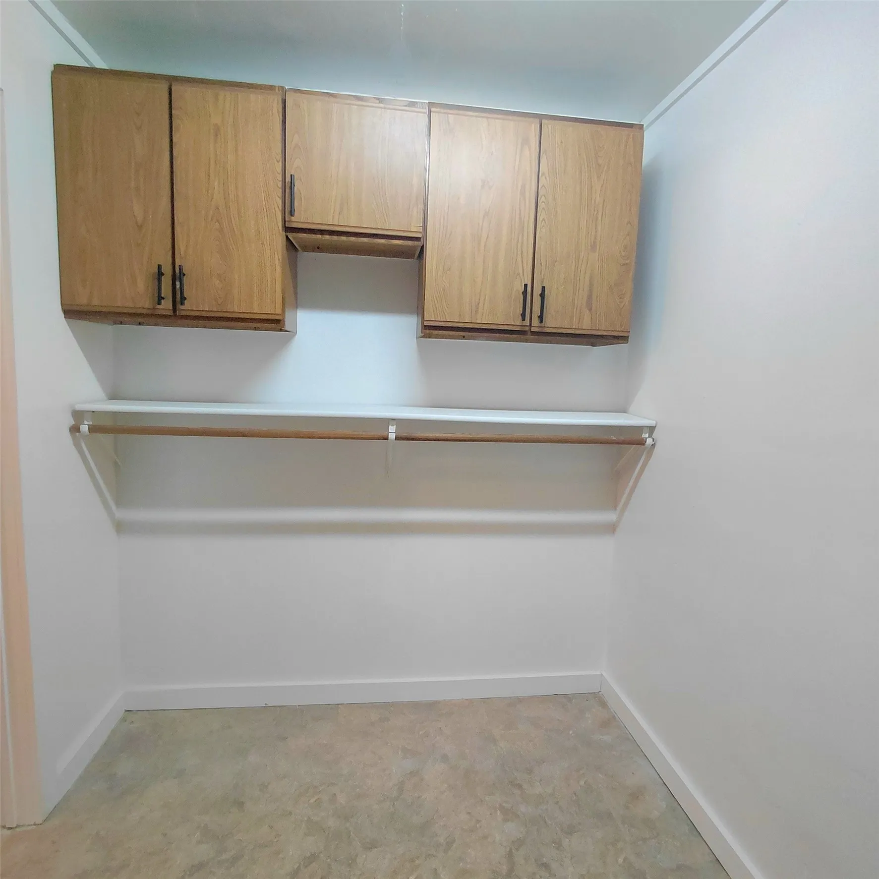 Wood-finish cabinetry with dark hardware, white shelving, hanging rod, and light-toned flooring