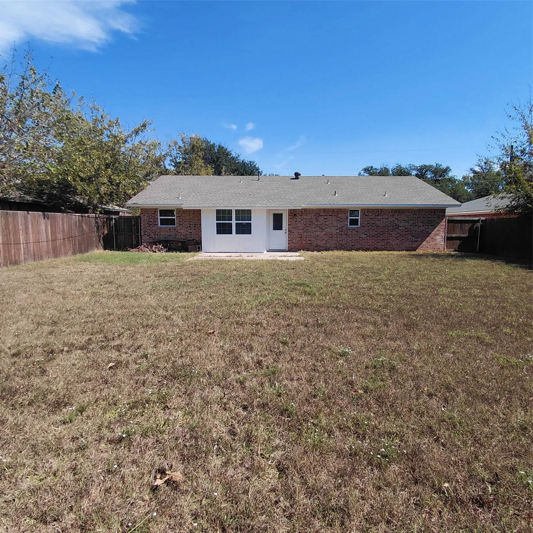 Expansive fenced backyard with a brick exterior, a patio, and a white paneled section with multiple windows