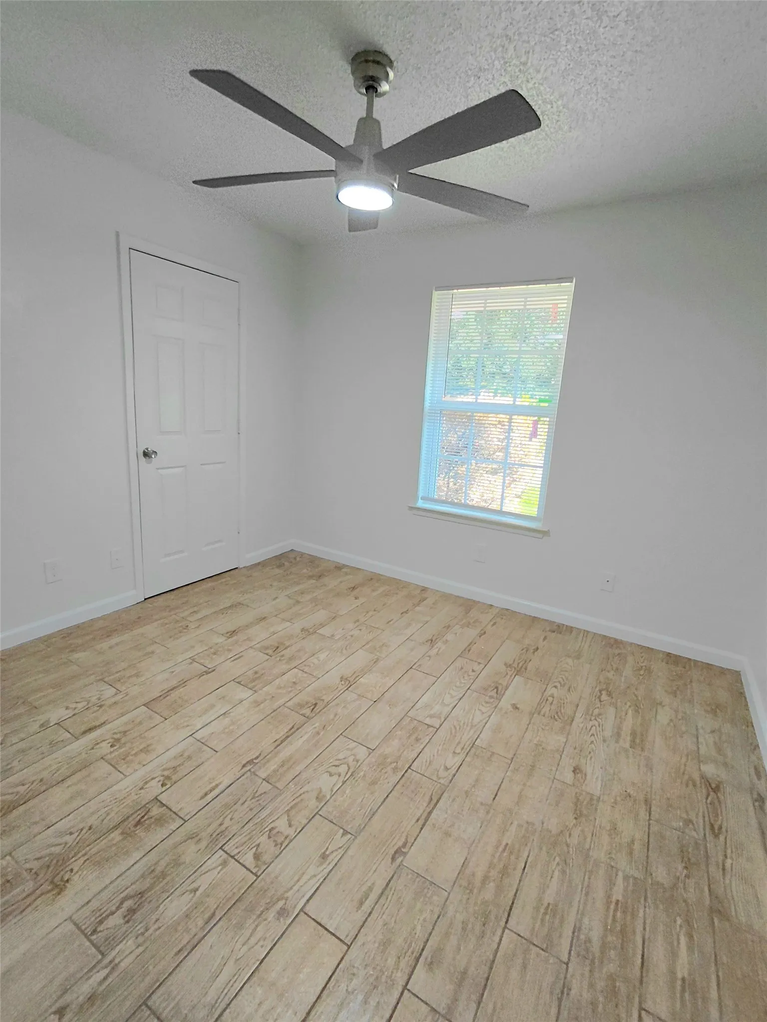 Wood-finish flooring, white walls, white trim, single window, and a ceiling fan with integrated lighting