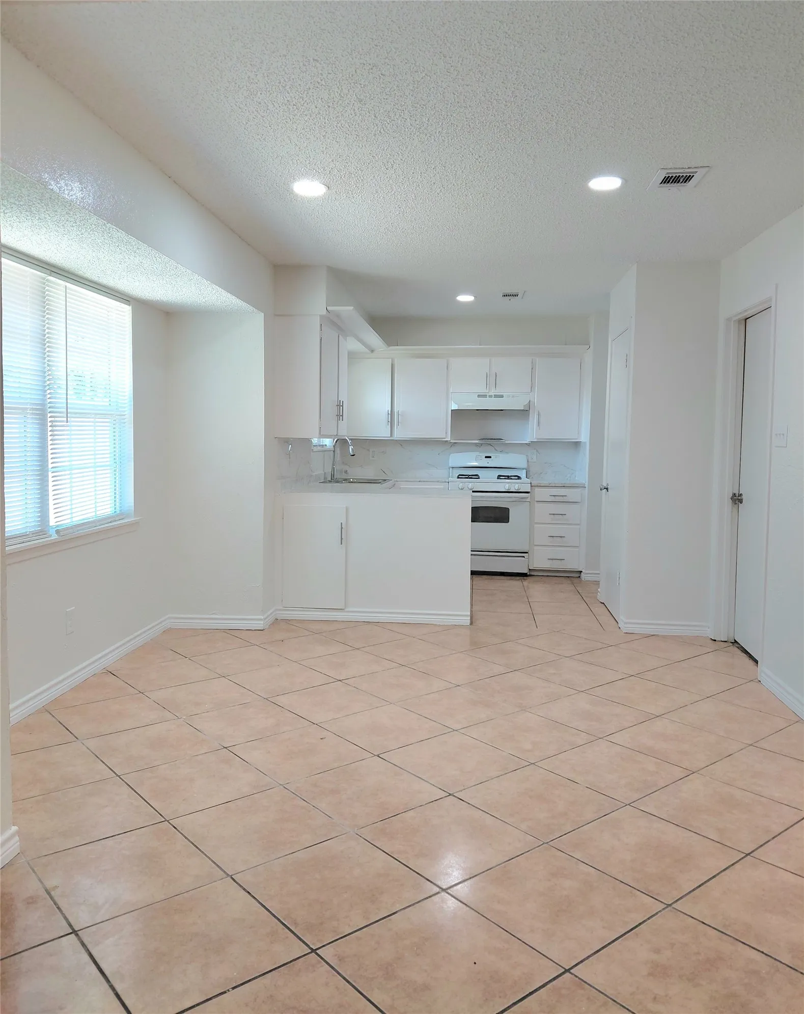 Tiled flooring, recessed lighting, white cabinetry, a built-in range, and a window with blinds
