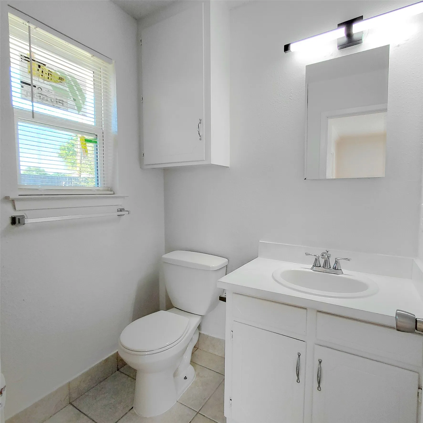 White vanity with an integrated sink and chrome faucet, under-cabinet storage, wall-mounted mirror, and overhead lighting