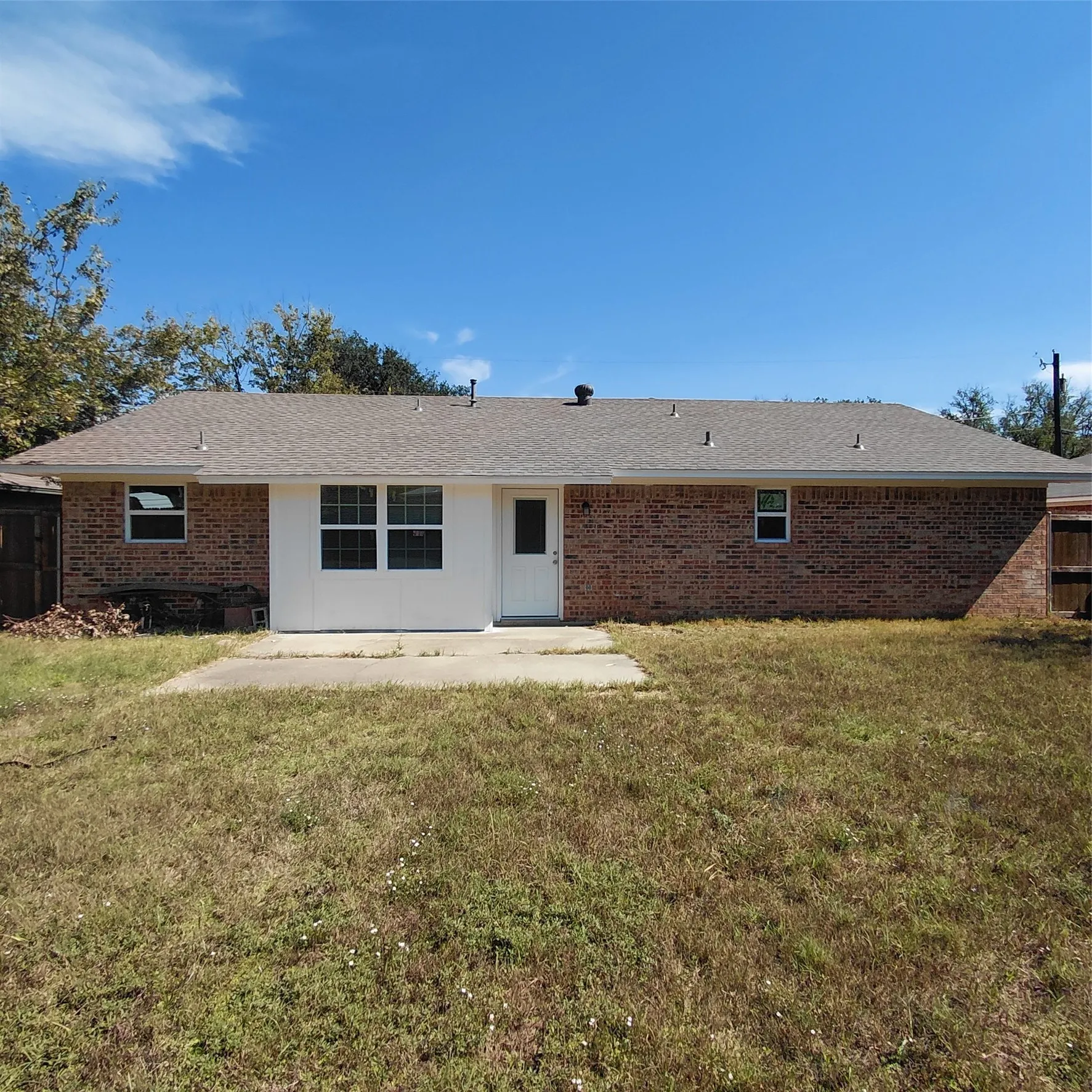 Brick exterior with a white rear entry door, multiple windows, and a concrete patio