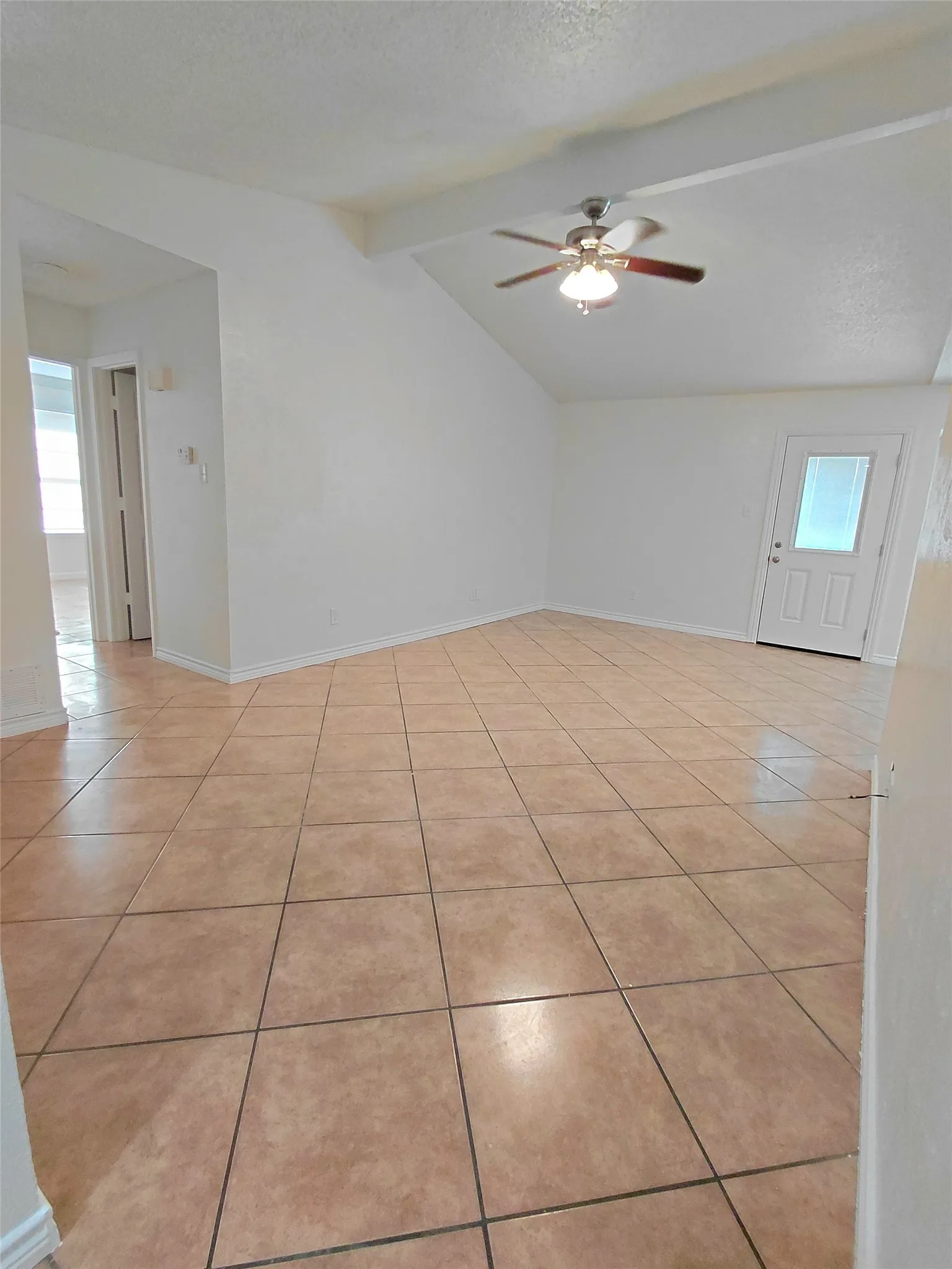 Vaulted ceiling with exposed beam, ceiling fan, ceramic tile flooring, and a white paneled door with an integrated window