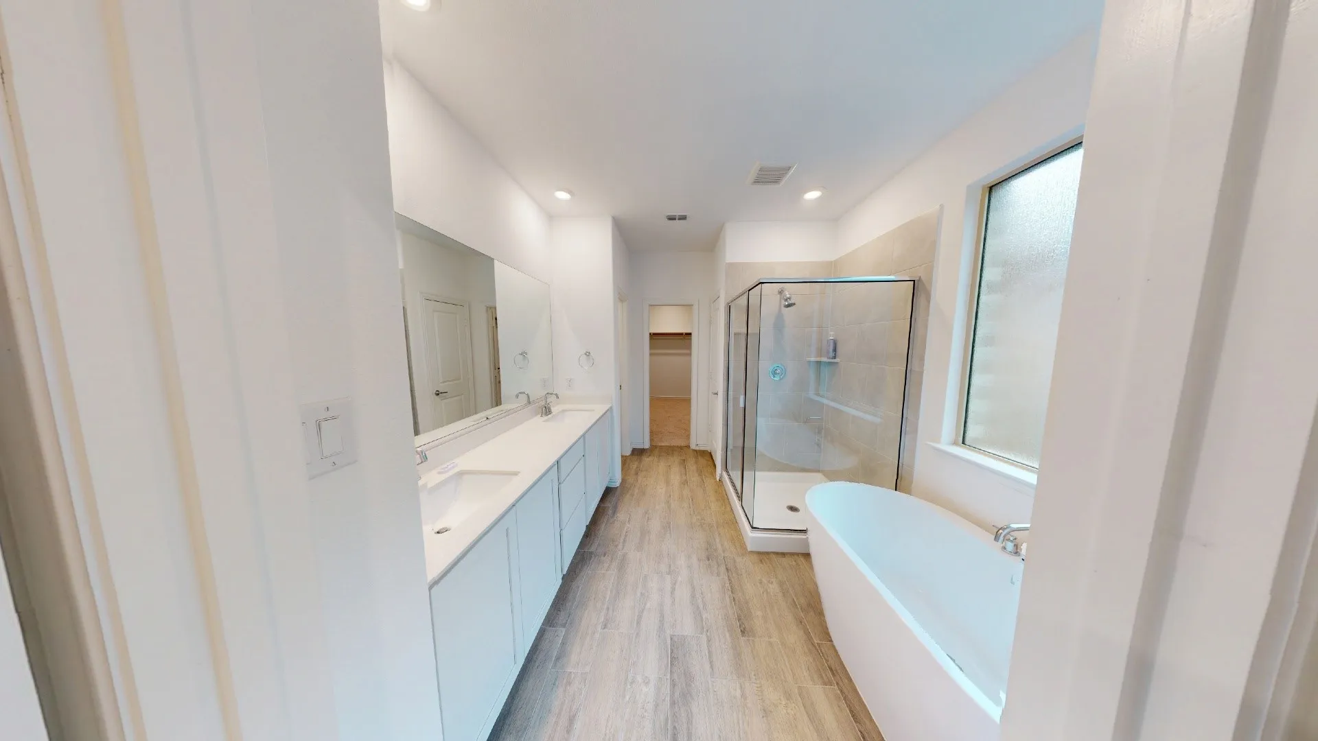 Dual vanity with rectangular undermount sinks, wood-finish flooring, glass-enclosed shower, freestanding soaking tub, and recessed lighting