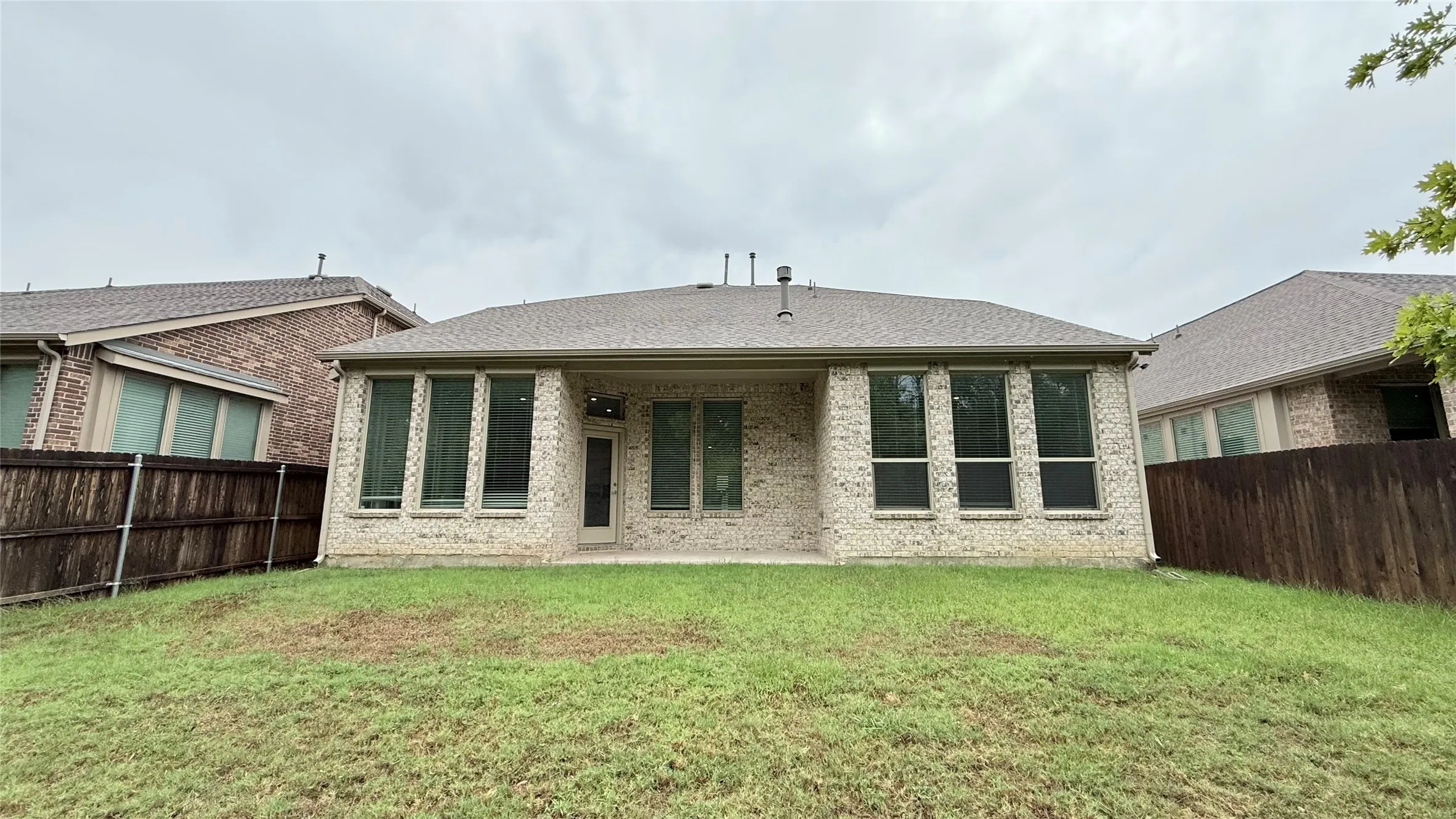 Expansive backyard with a manicured lawn, brick exterior, covered patio, and privacy fencing