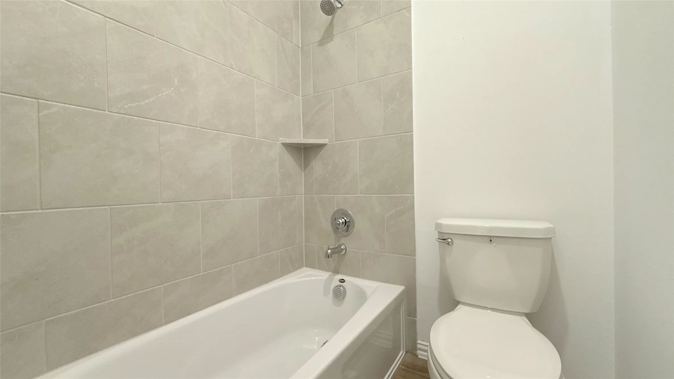 Bathtub with integrated shelving, chrome fixtures, and neutral wall tiling