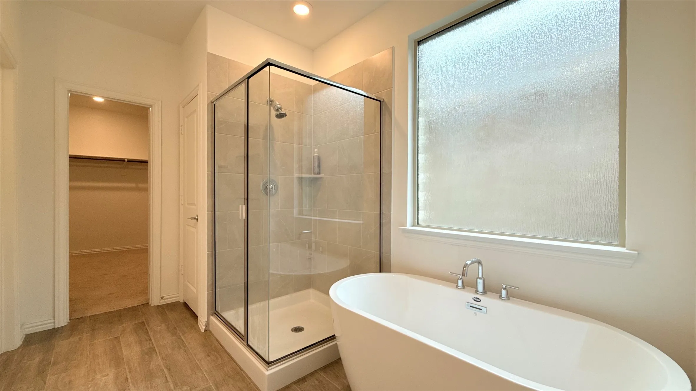 Freestanding soaking tub with chrome fixtures, glass-enclosed shower with tile surround, and wood-finish flooring