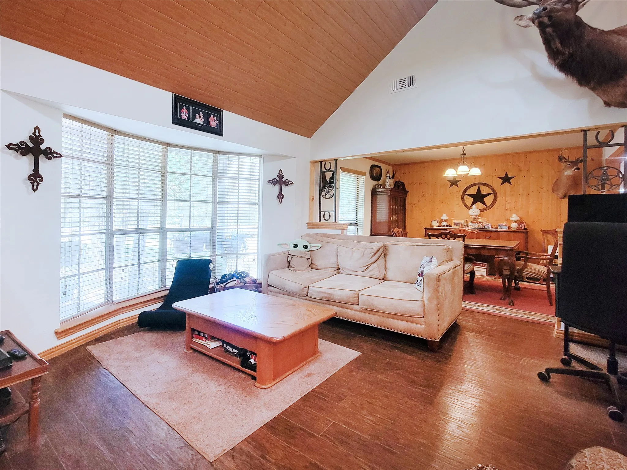 Vaulted ceiling with wood-finish paneling, expansive bay window with blinds, wood-finish flooring, and open-concept dining area
