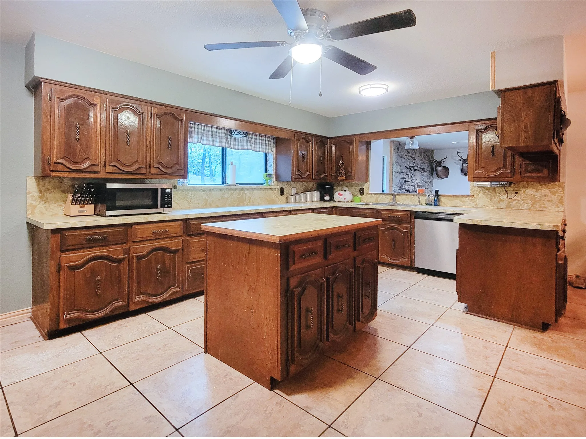 Spacious kitchen featuring extensive wood cabinetry, a central island, tile flooring, and light-colored countertops with matching backsplash