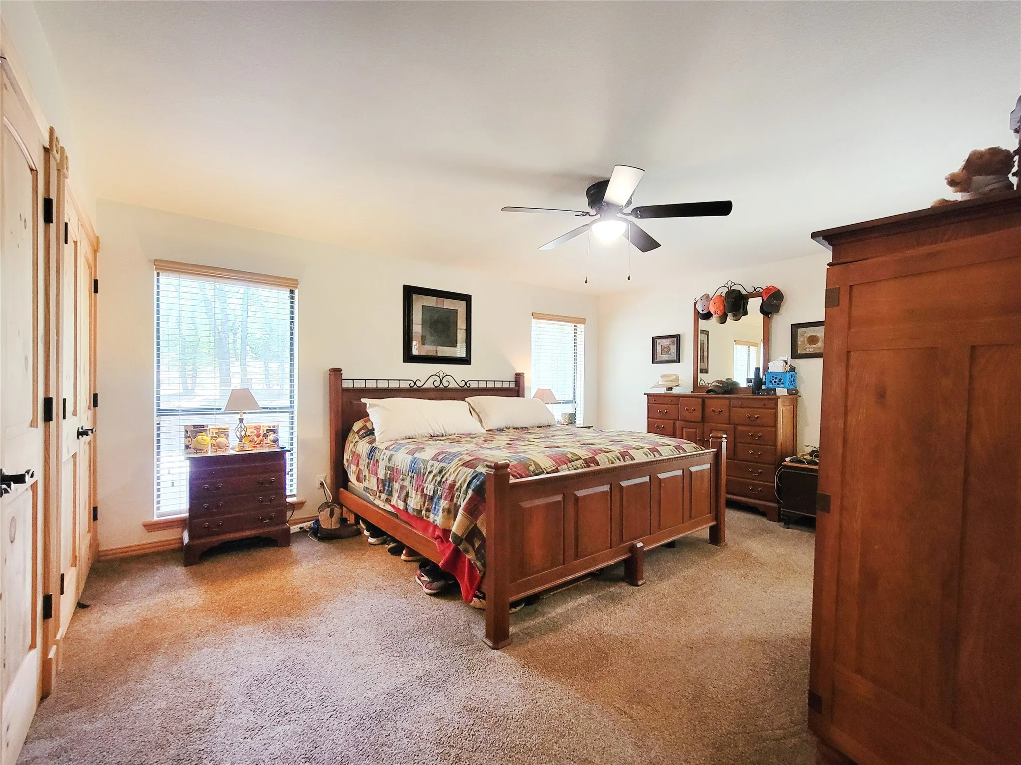 Carpeted bedroom with a ceiling fan, dual windows, and light wood-finish double doors