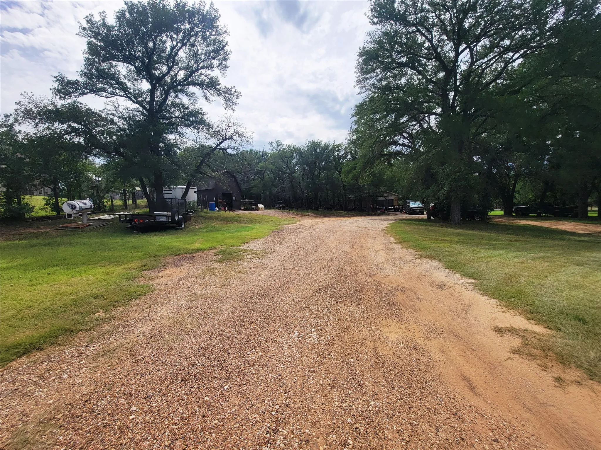 Gravel driveway with mature trees and a rustic barn