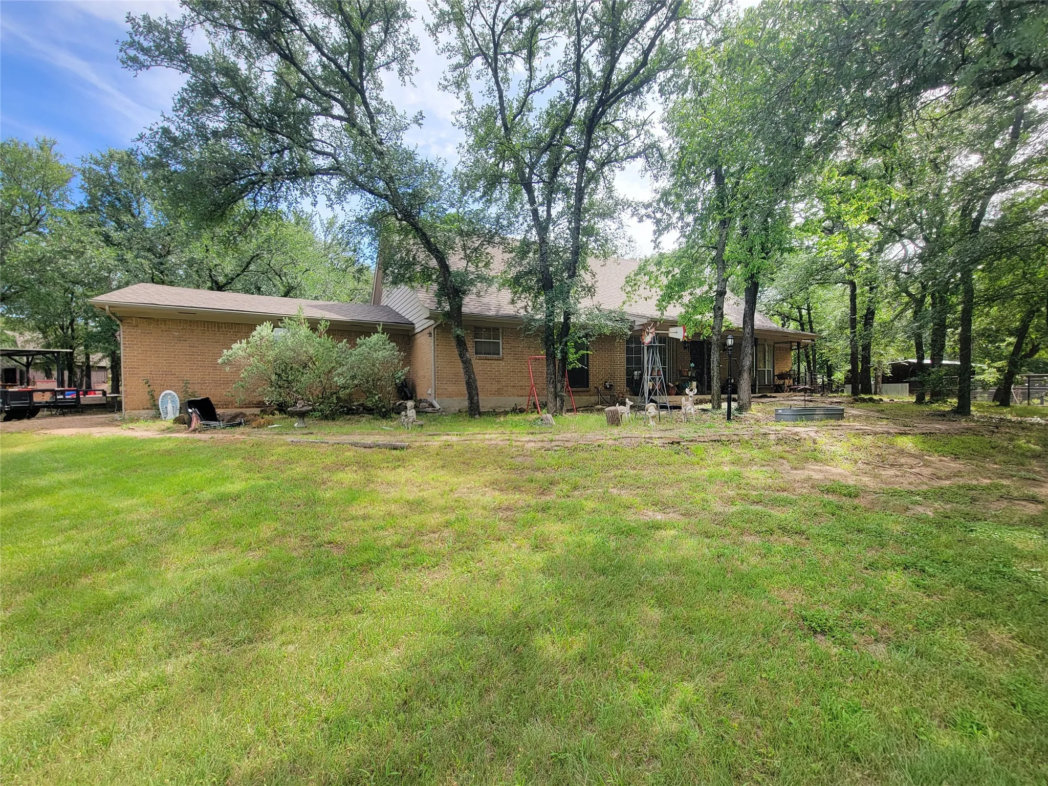 Brick exterior residence with a covered patio, extensive lawn, and mature trees