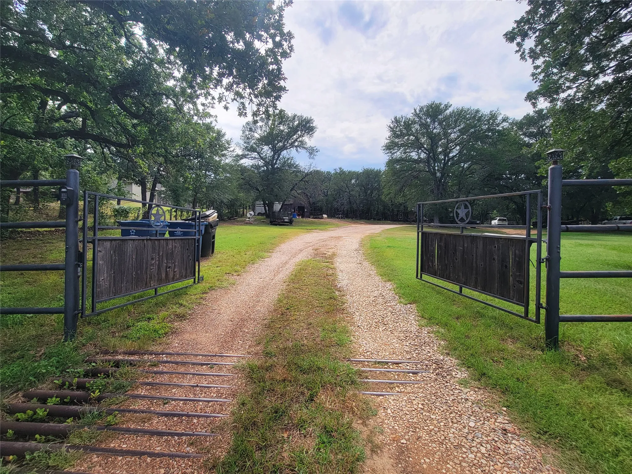 Gated entrance featuring a gravel drive, cattle guard, and mature trees