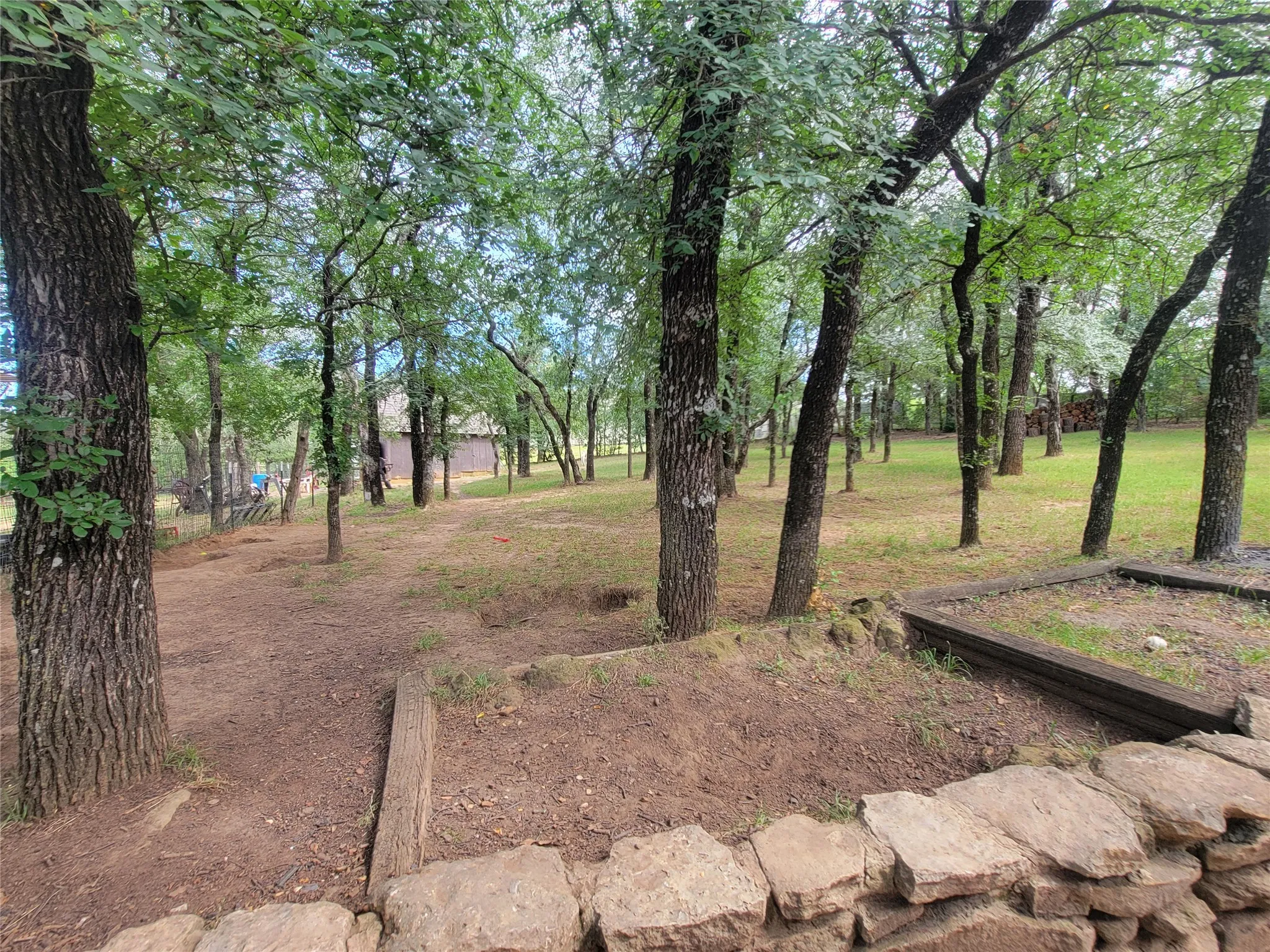 Wooded grounds featuring mature trees and a stone retaining wall