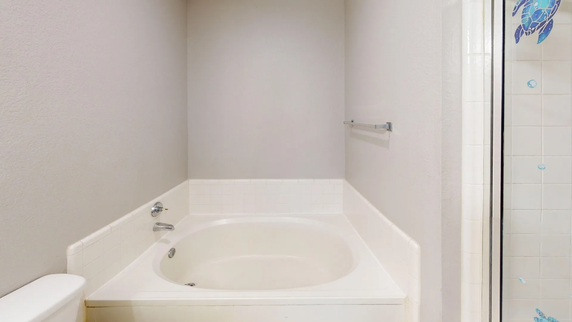 Built-in soaking tub with white tile surround, chrome faucet hardware, and a glass-enclosed shower stall