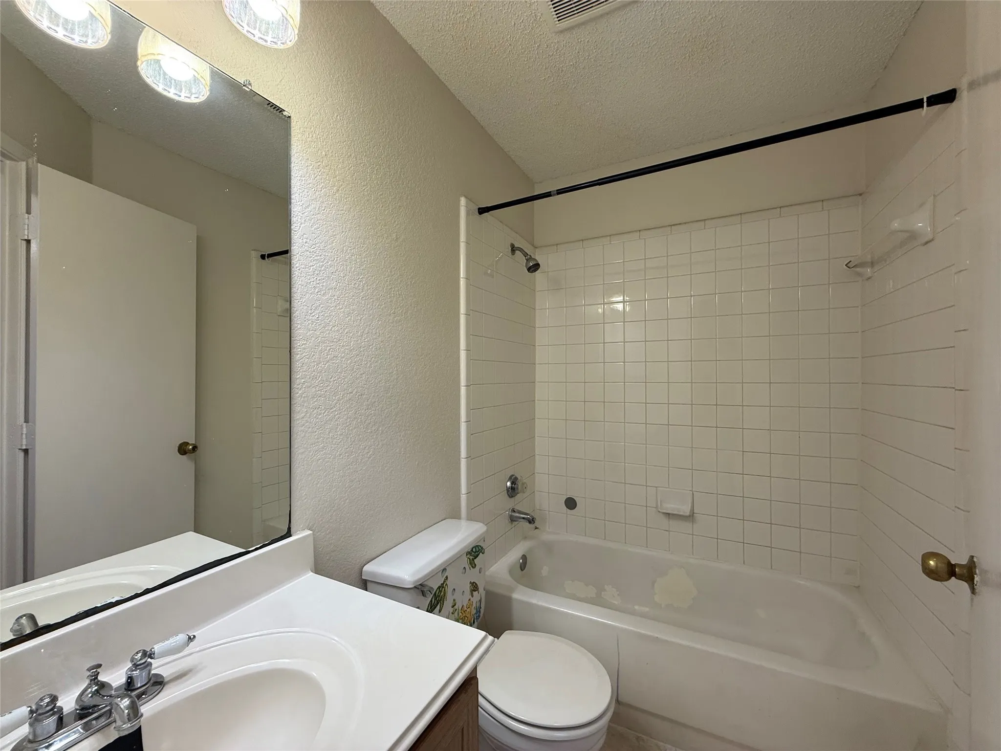 Bathroom featuring a vanity with a white countertop and oval sink, a wall-mounted mirror, three-light overhead fixture, and a tub-shower combination with white wall tile