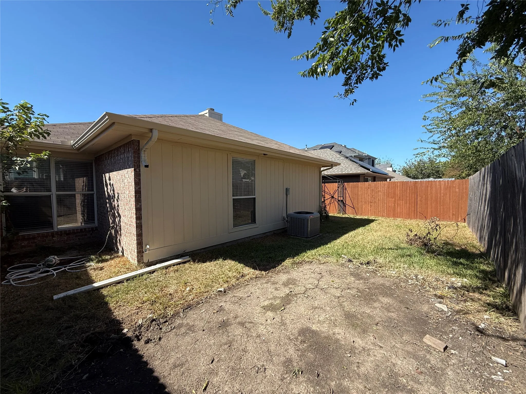 Rear exterior featuring a brick and panel siding facade, grass yard, and wood privacy fencing