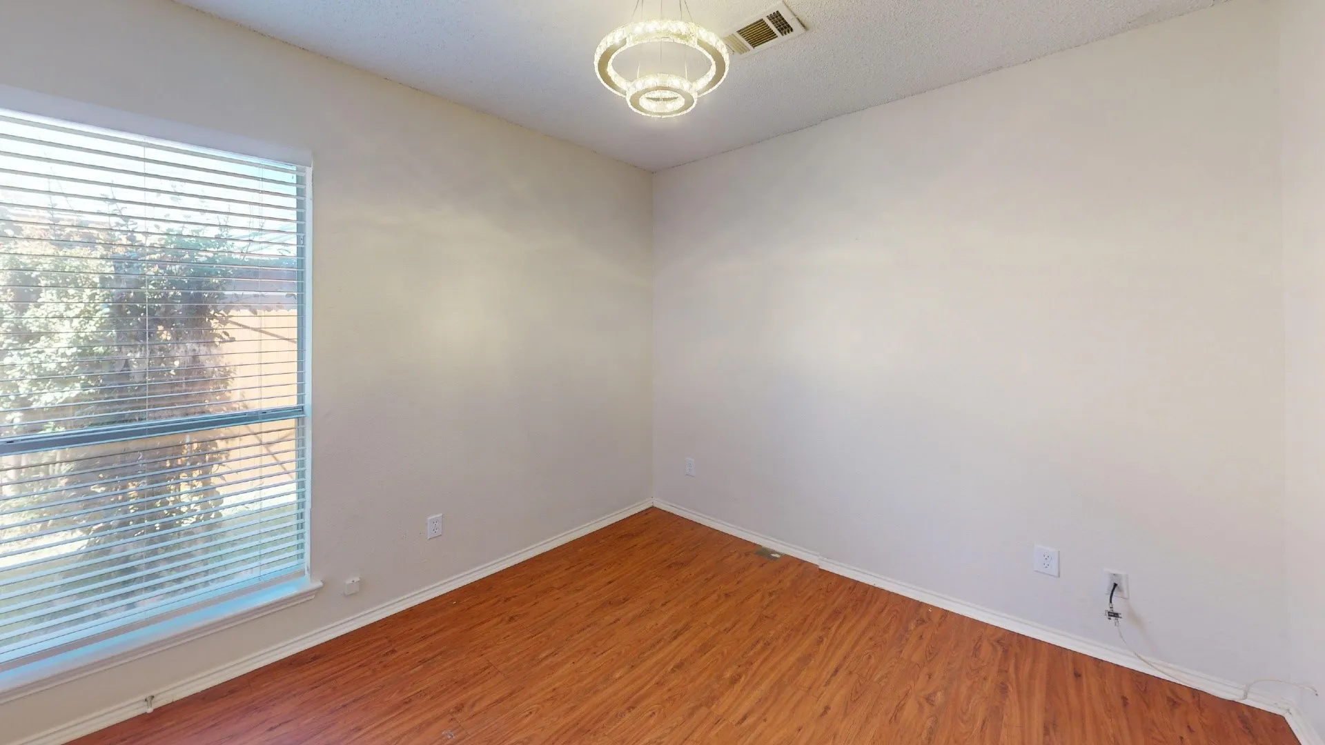Room featuring wood-finish flooring, a contemporary circular pendant light fixture, and horizontal slat window blinds