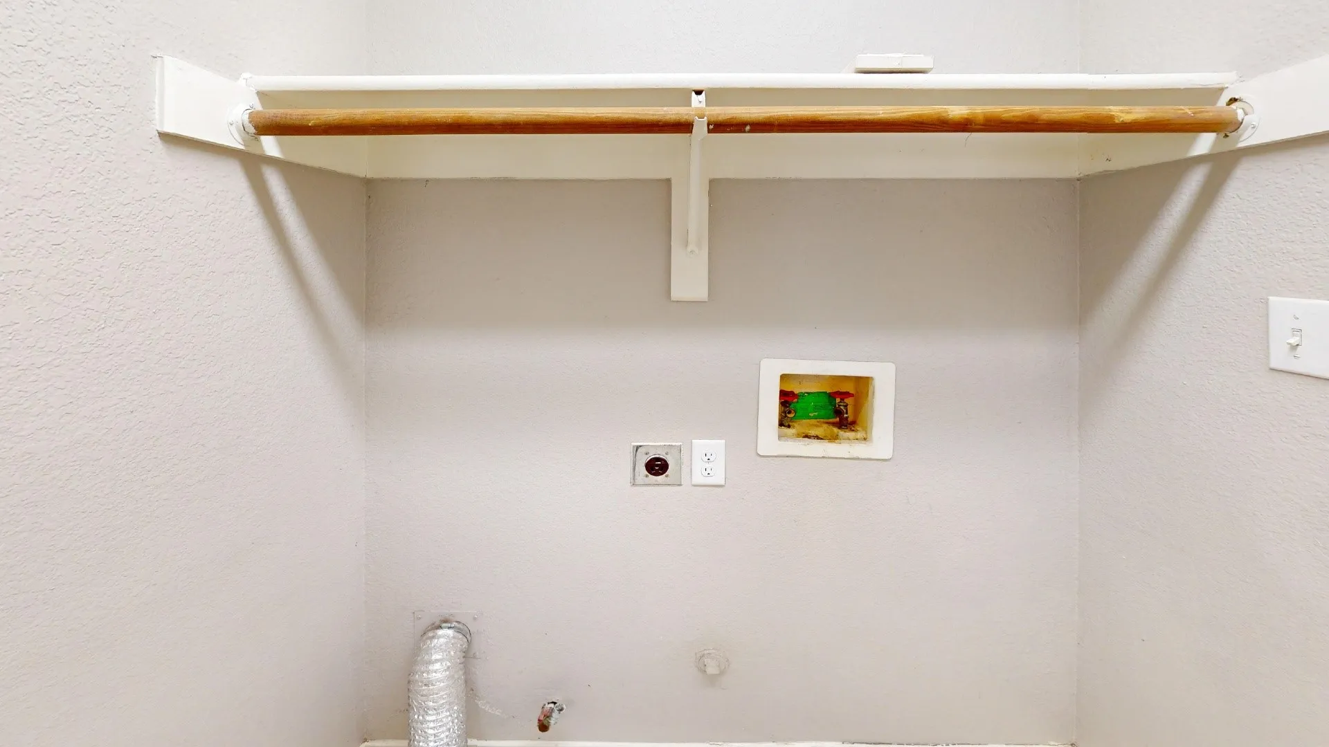 Dedicated laundry area featuring a recessed utility box, dedicated electrical outlet, and an overhead shelf with a mounted garment rod