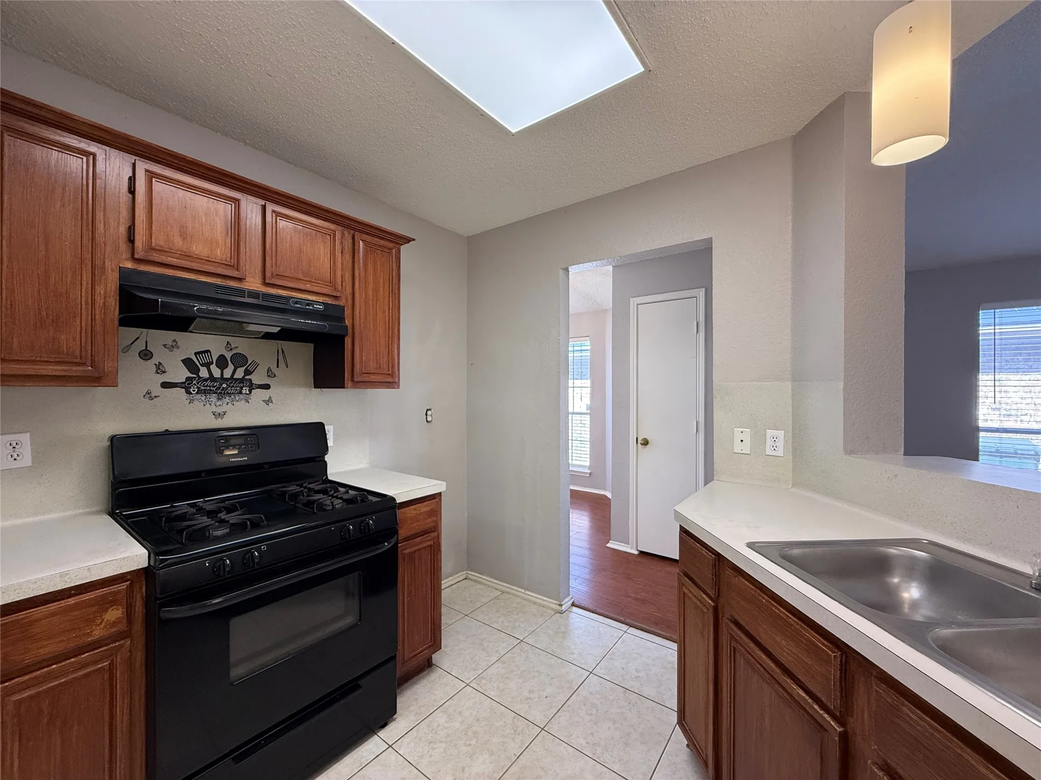 Kitchen featuring wood cabinetry, solid-surface countertops, dual-basin stainless steel sink, black range, and ceramic tile flooring