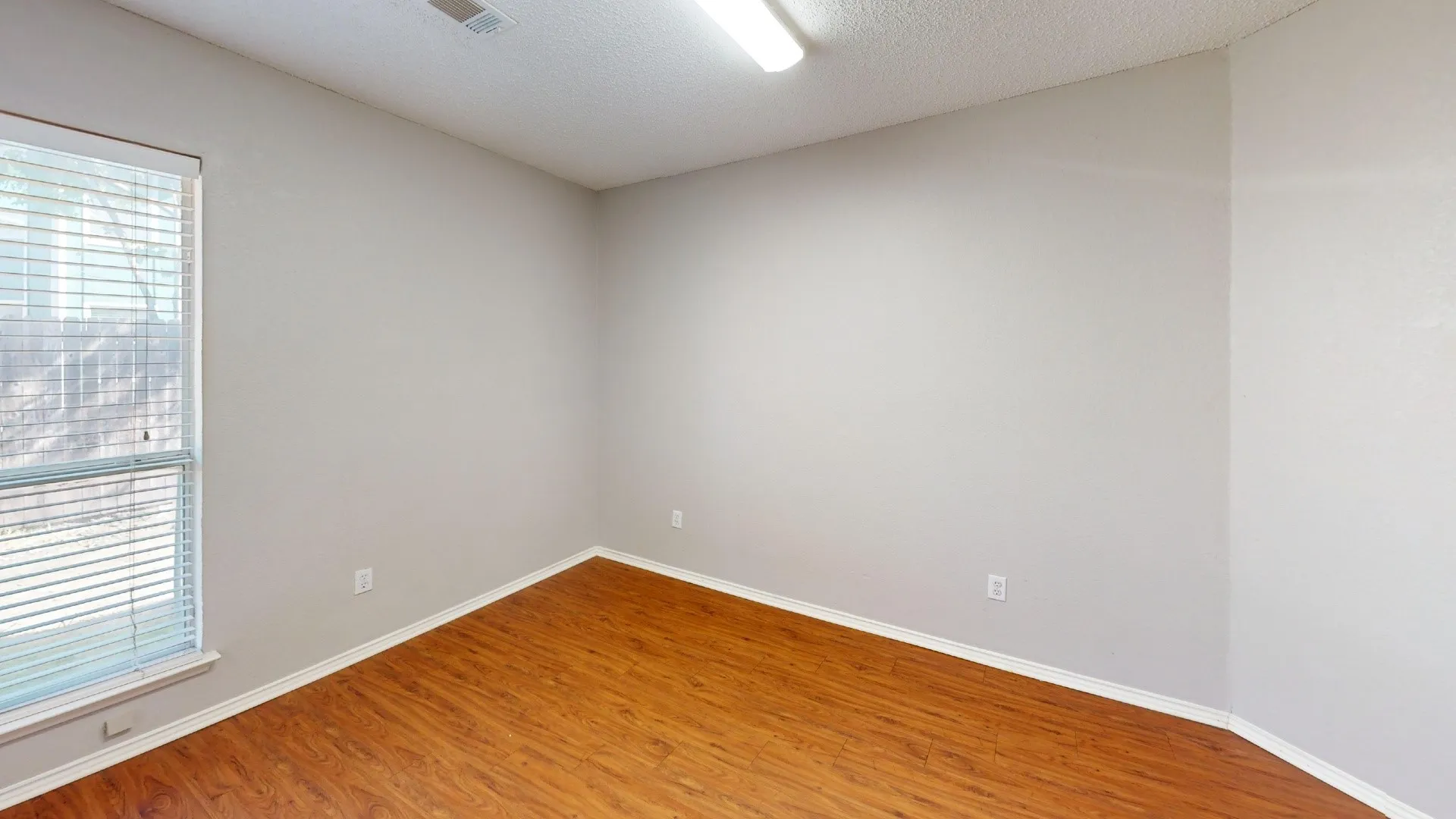Neutral-toned walls, wood-finish flooring, and single-pane window with horizontal blinds