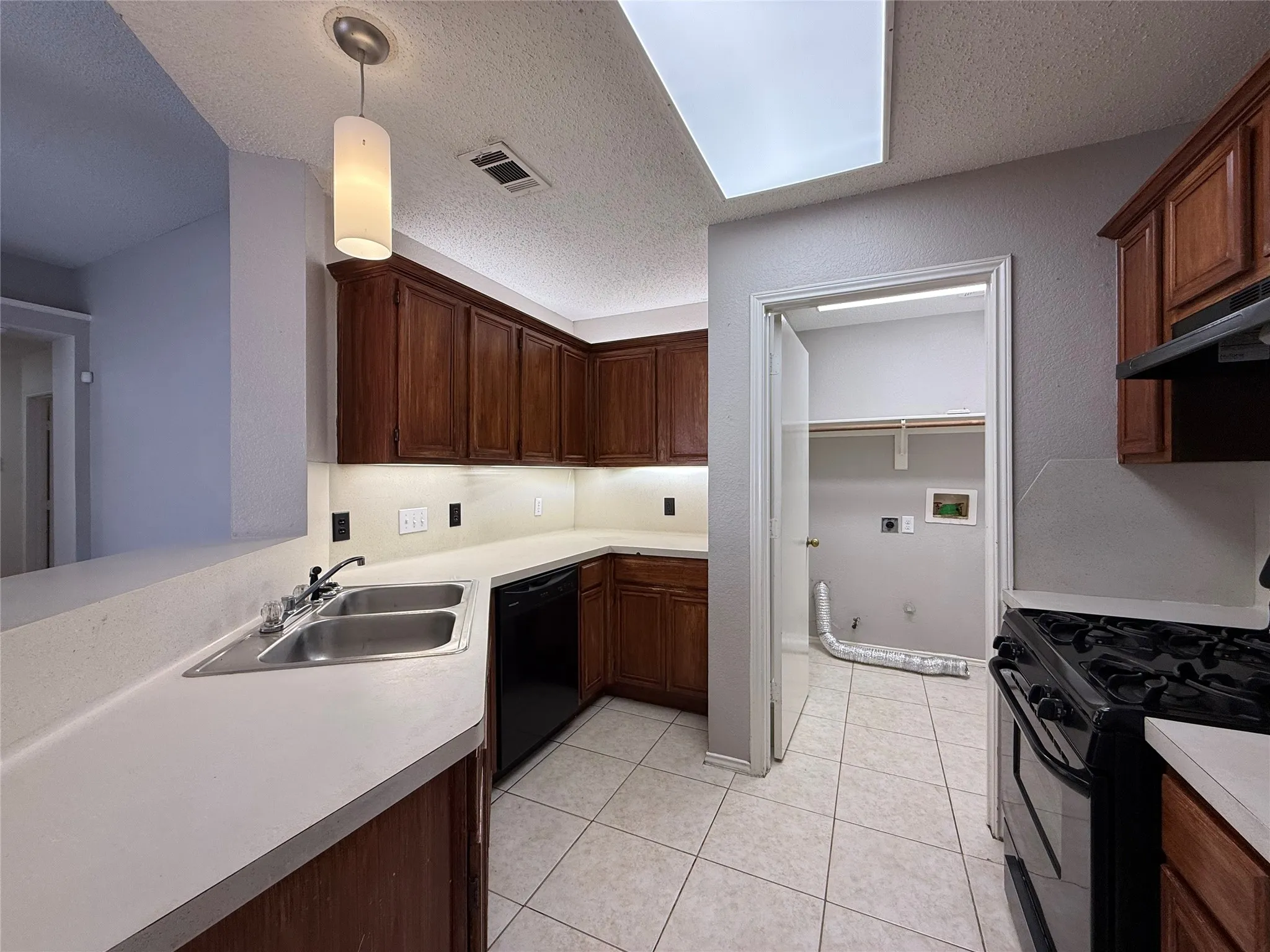 Kitchen featuring stained wood cabinetry, solid surface countertops, dual-basin stainless steel sink, integrated recessed lighting, and tile flooring