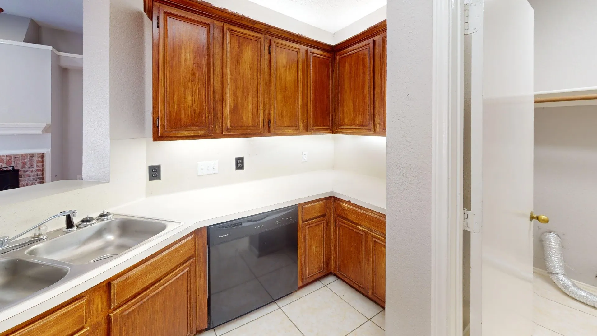 Kitchen featuring stained wood cabinetry, solid-surface countertops, dual-basin stainless steel sink, black dishwasher, and tile flooring