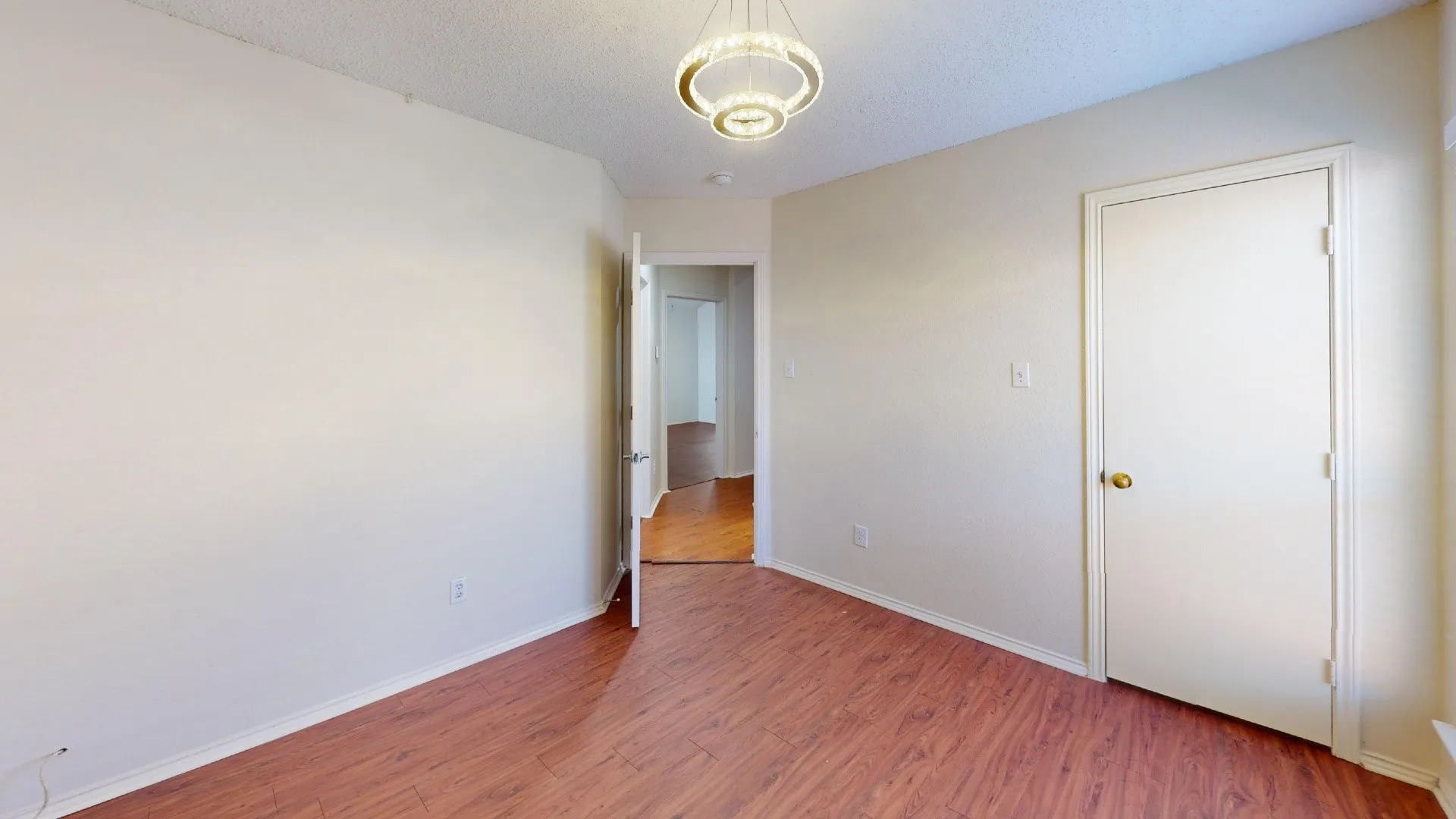 Neutral-toned interior space featuring wood-finish flooring, a modern tiered chandelier, and a solid-core interior door