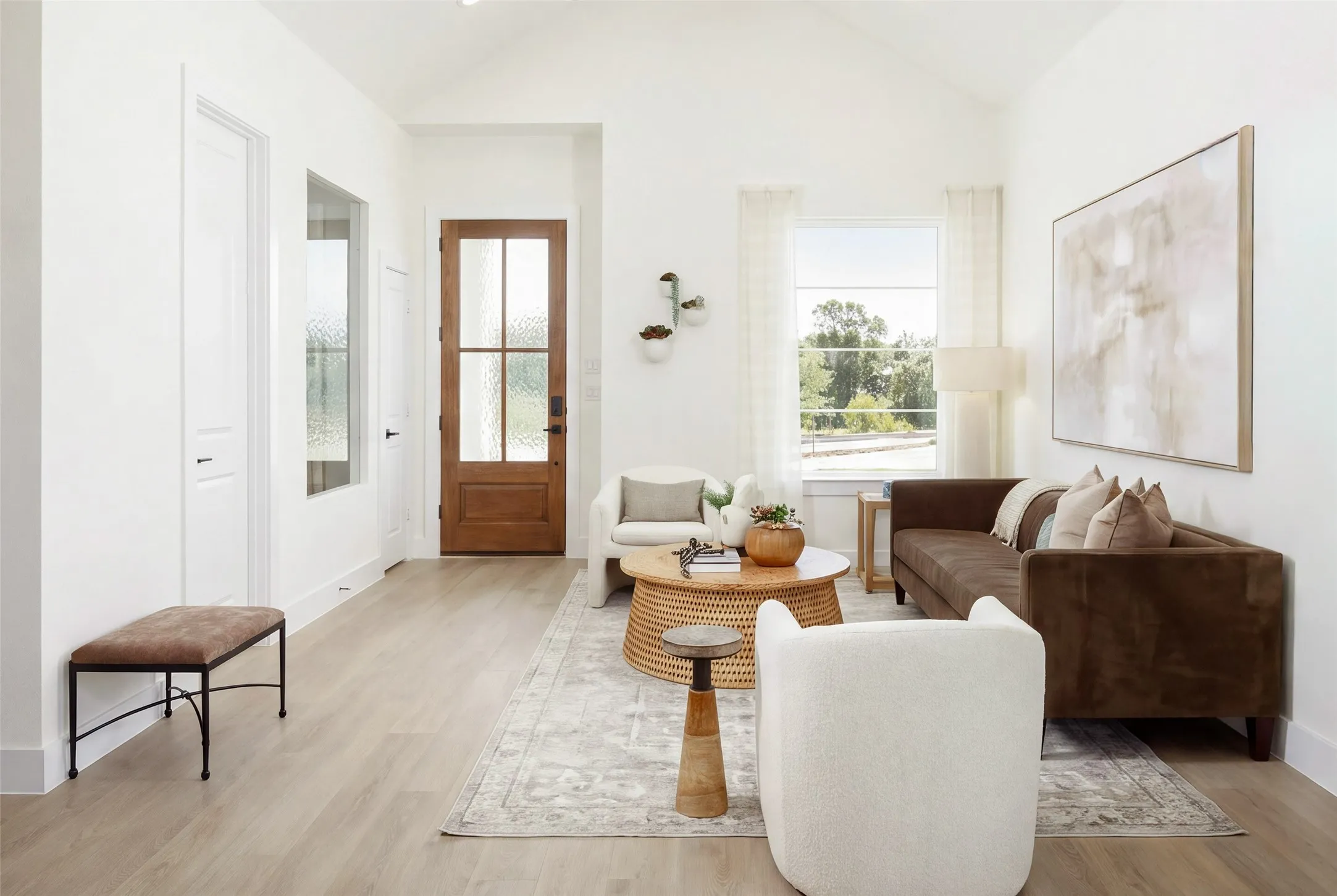 Vaulted white ceiling, wood-finish flooring, white walls, wood entry door with frosted glass panels, and a large window with white trim