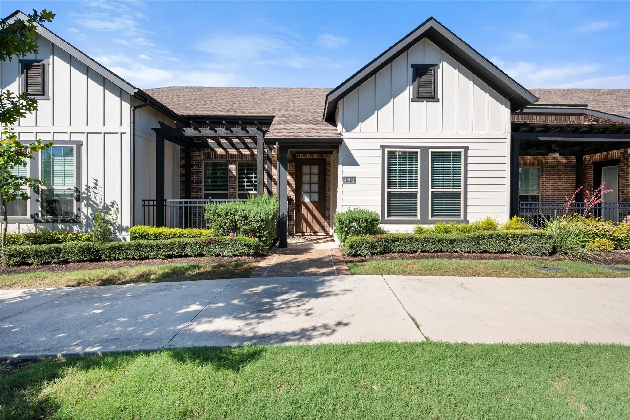 Board and batten siding, brick accents, a gabled roofline, front entry pergola, and neatly trimmed landscaping define the exterior