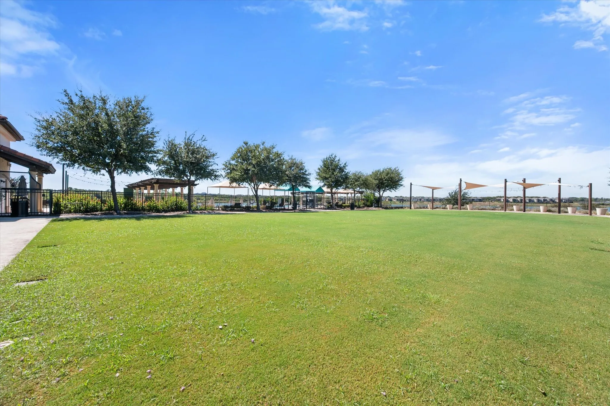 Expansive green space featuring scattered mature trees, a built-in pergola, and shade structures