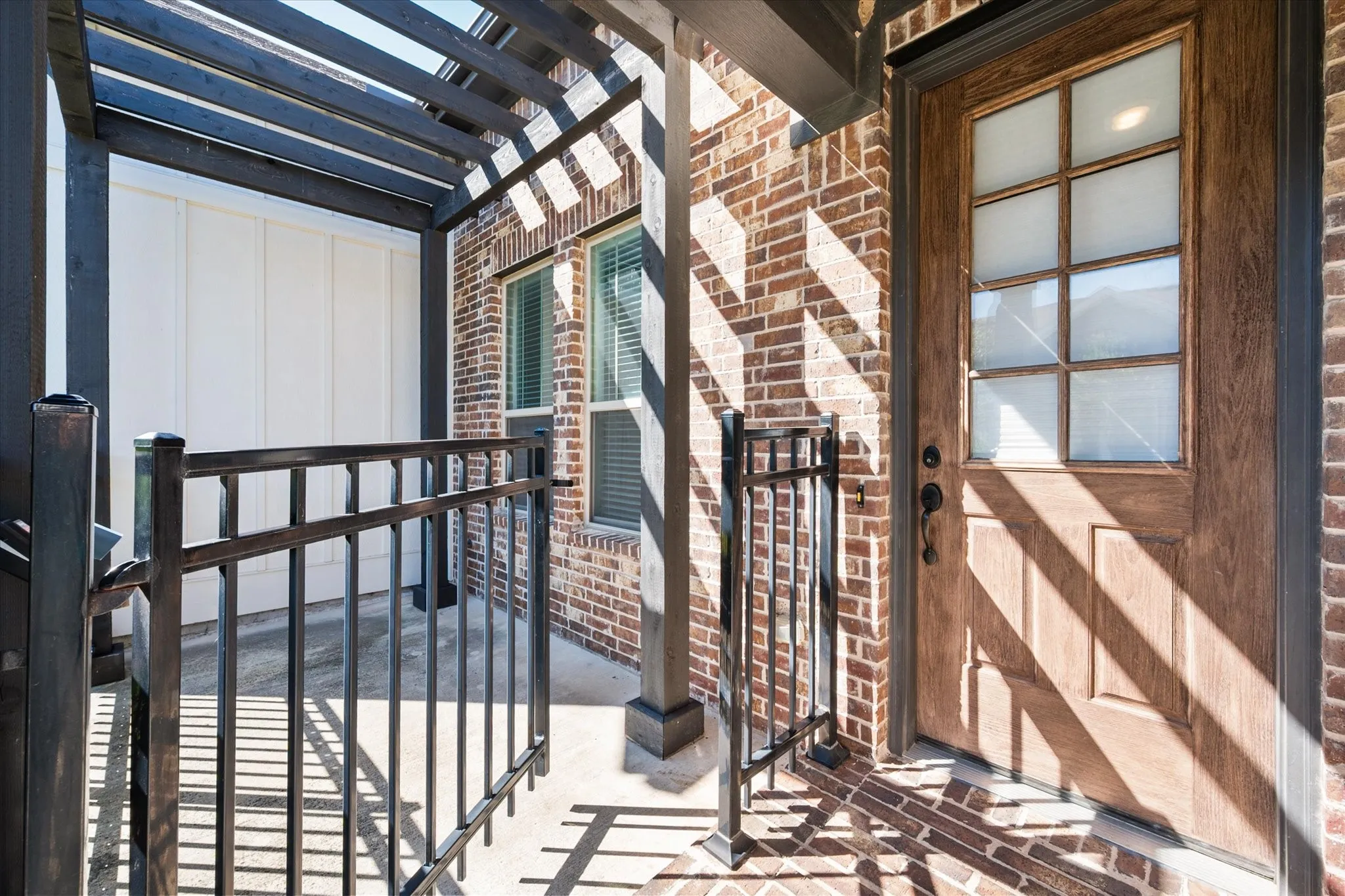 Brick exterior with a wood-finish entry door, decorative glass inserts, and a pergola-covered porch