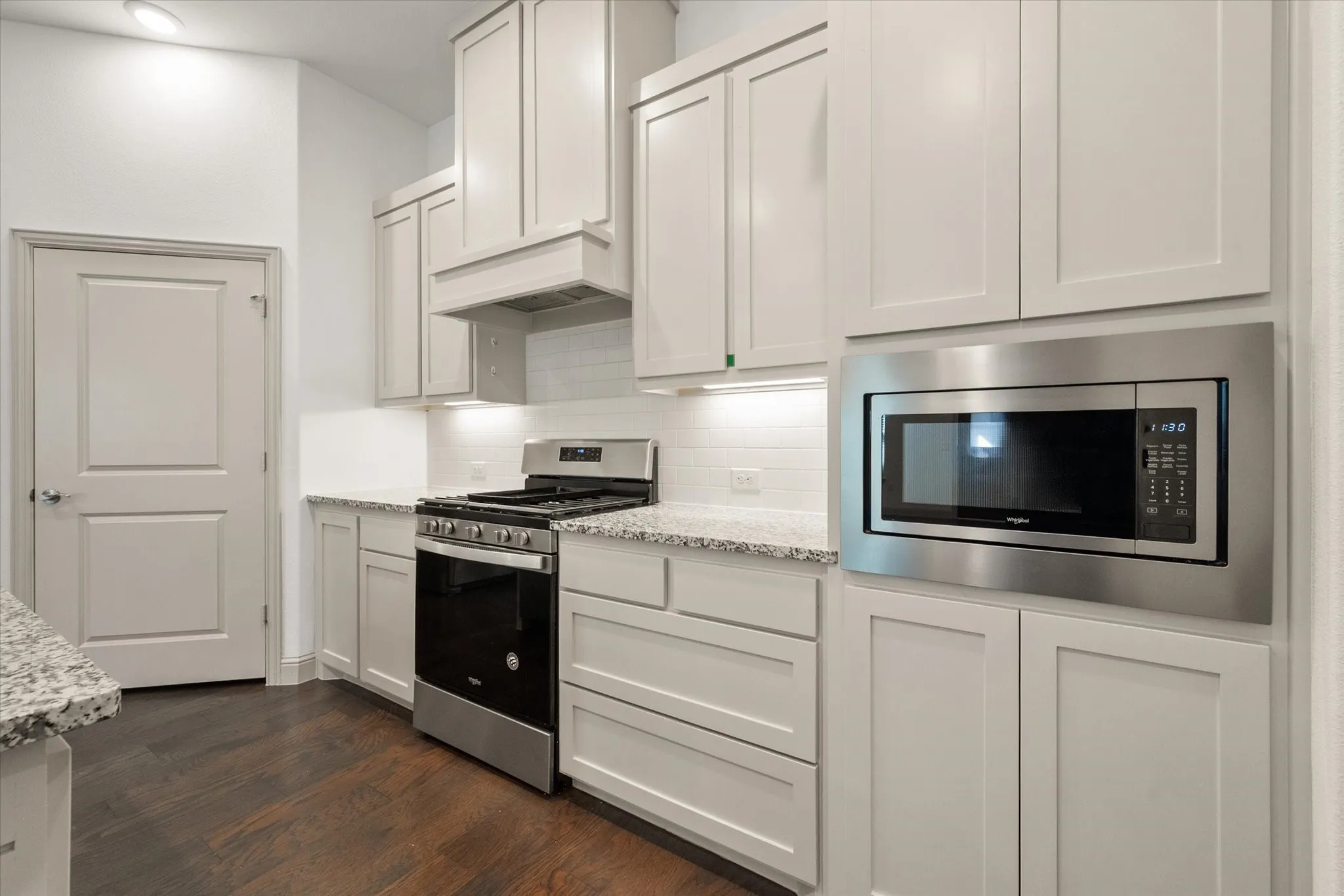 White shaker cabinetry, stainless steel appliances, granite countertops, subway tile backsplash, and wood-finish flooring