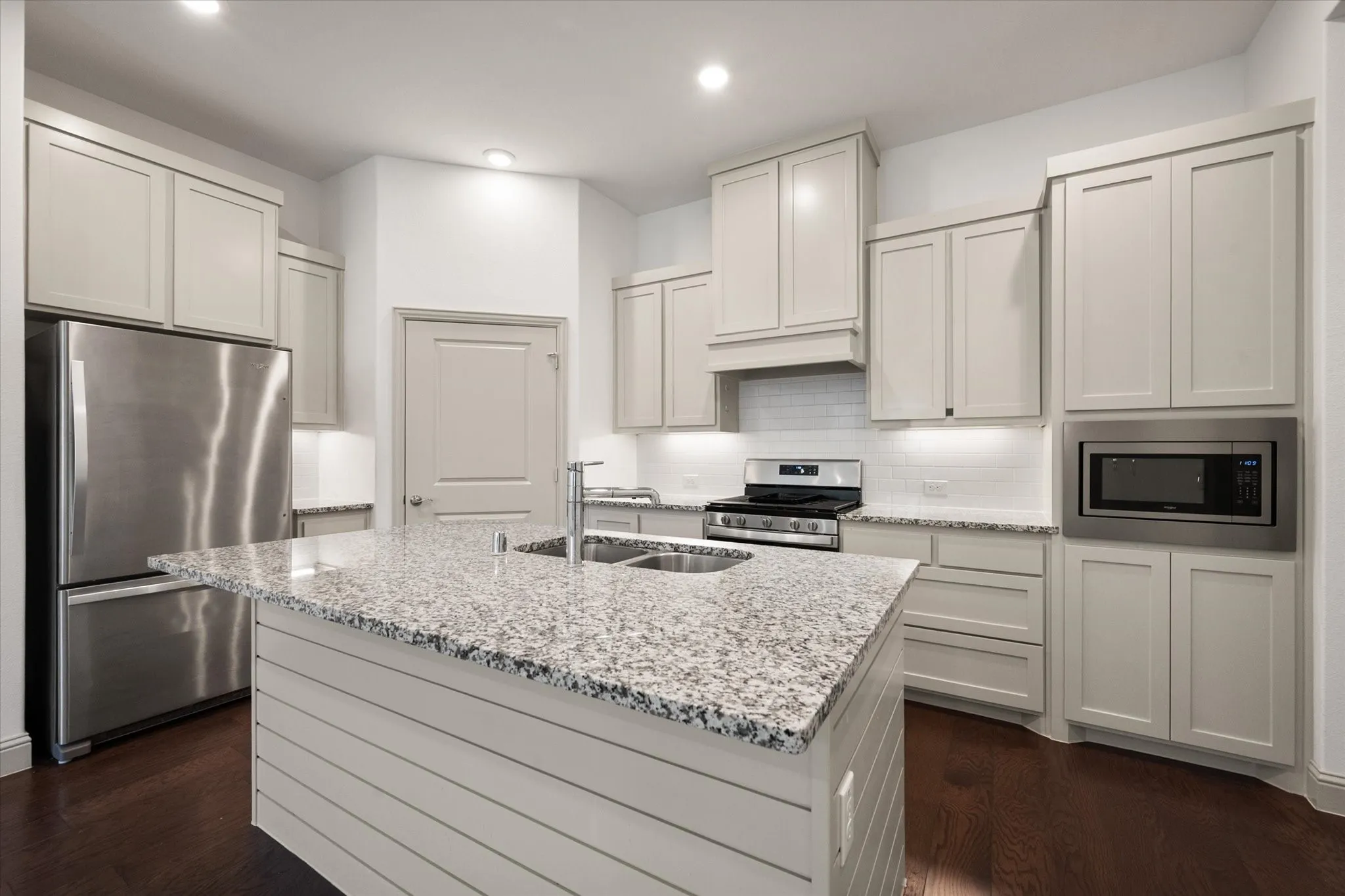 Kitchen featuring a central island with dual sinks, light-toned cabinetry, stainless steel appliances, and wood-finish flooring