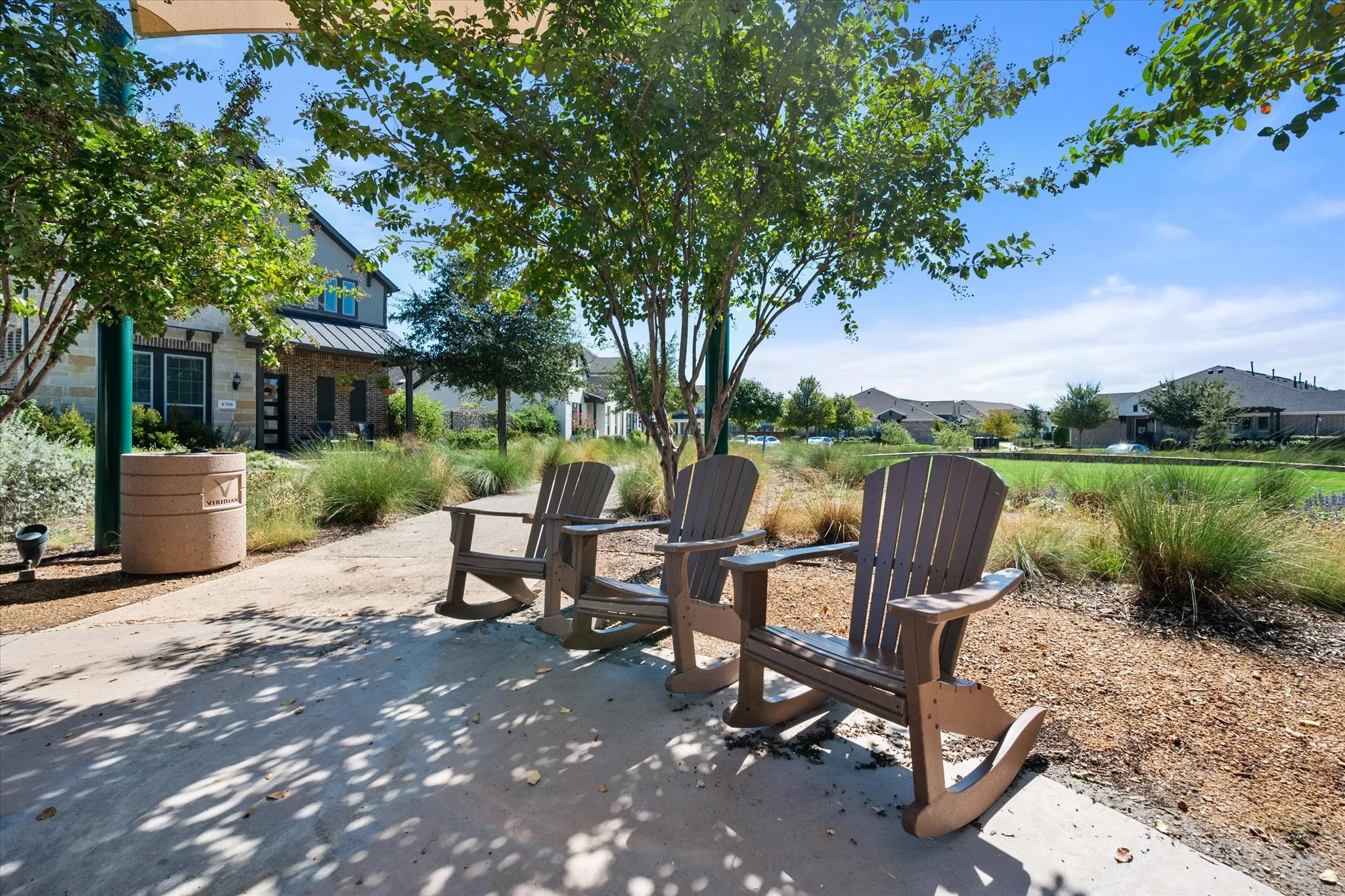 Outdoor seating area featuring three Adirondack-style rocking chairs, a paved pathway, and mature landscaping