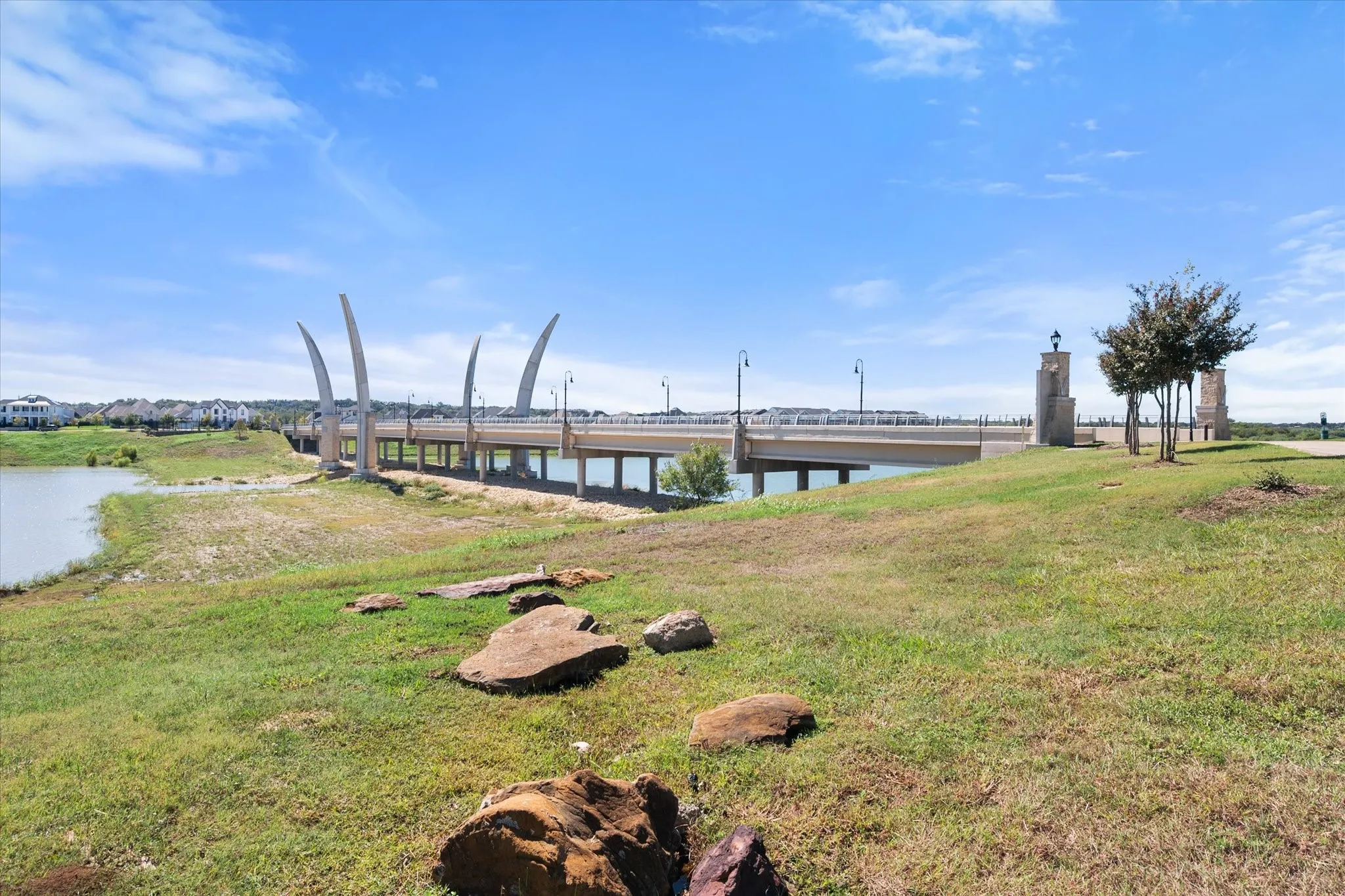 Expansive green space featuring large natural boulders, a manicured tree, and waterside frontage with a bridge structure
