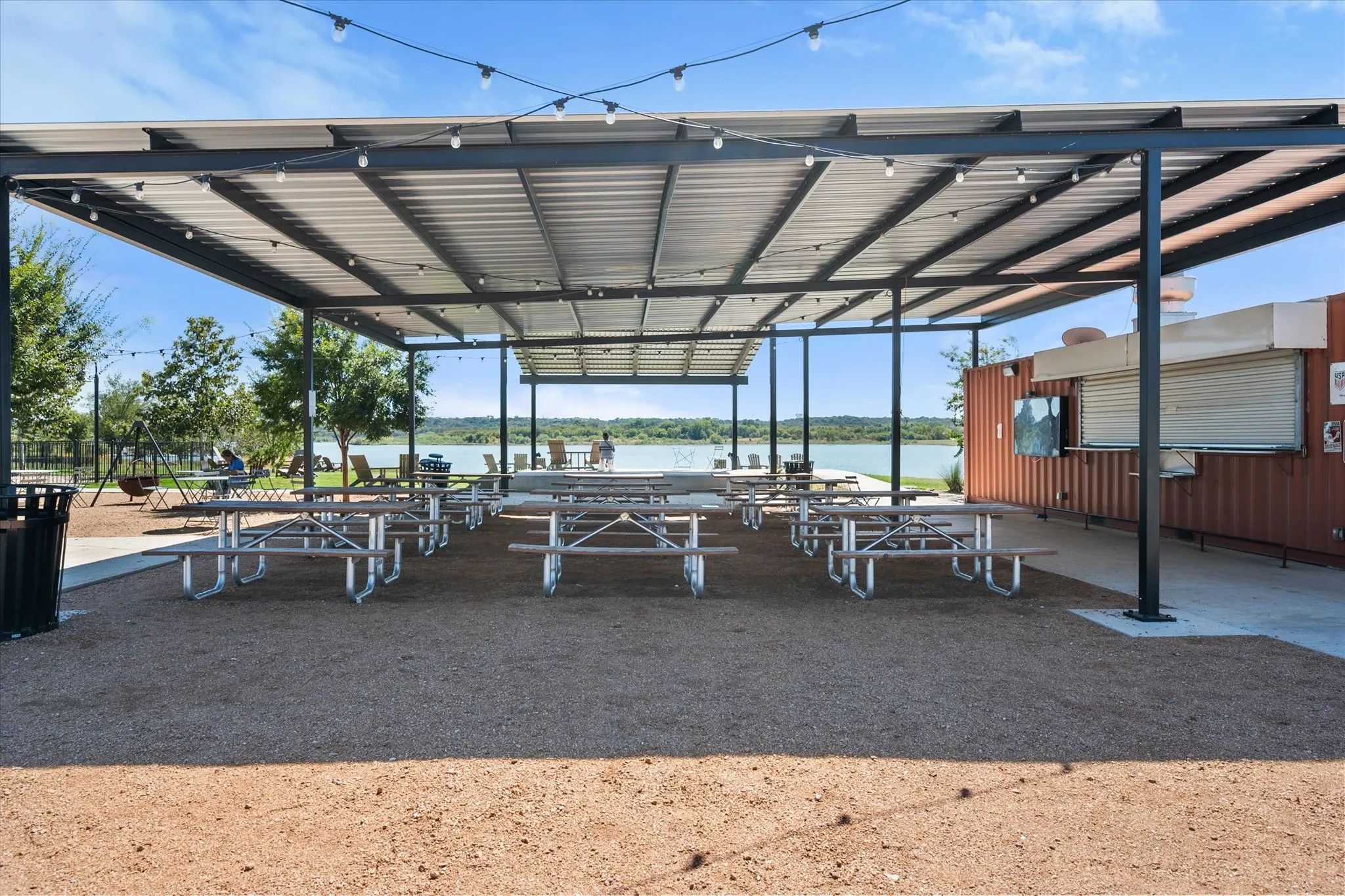 Expansive outdoor patio featuring a large metal-frame canopy, string lighting, and direct water frontage