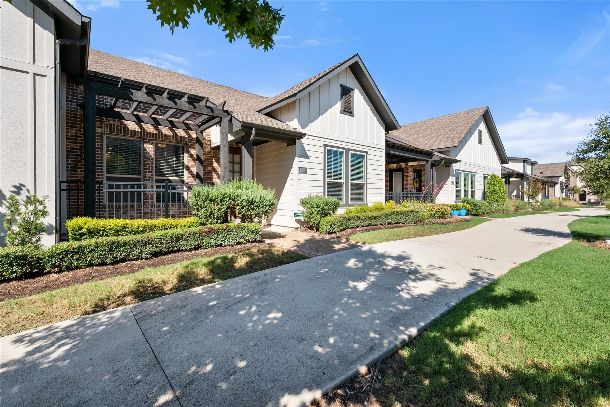 Modern facade with gabled roof lines, board and batten siding, brick accents, and a dark-stained pergola