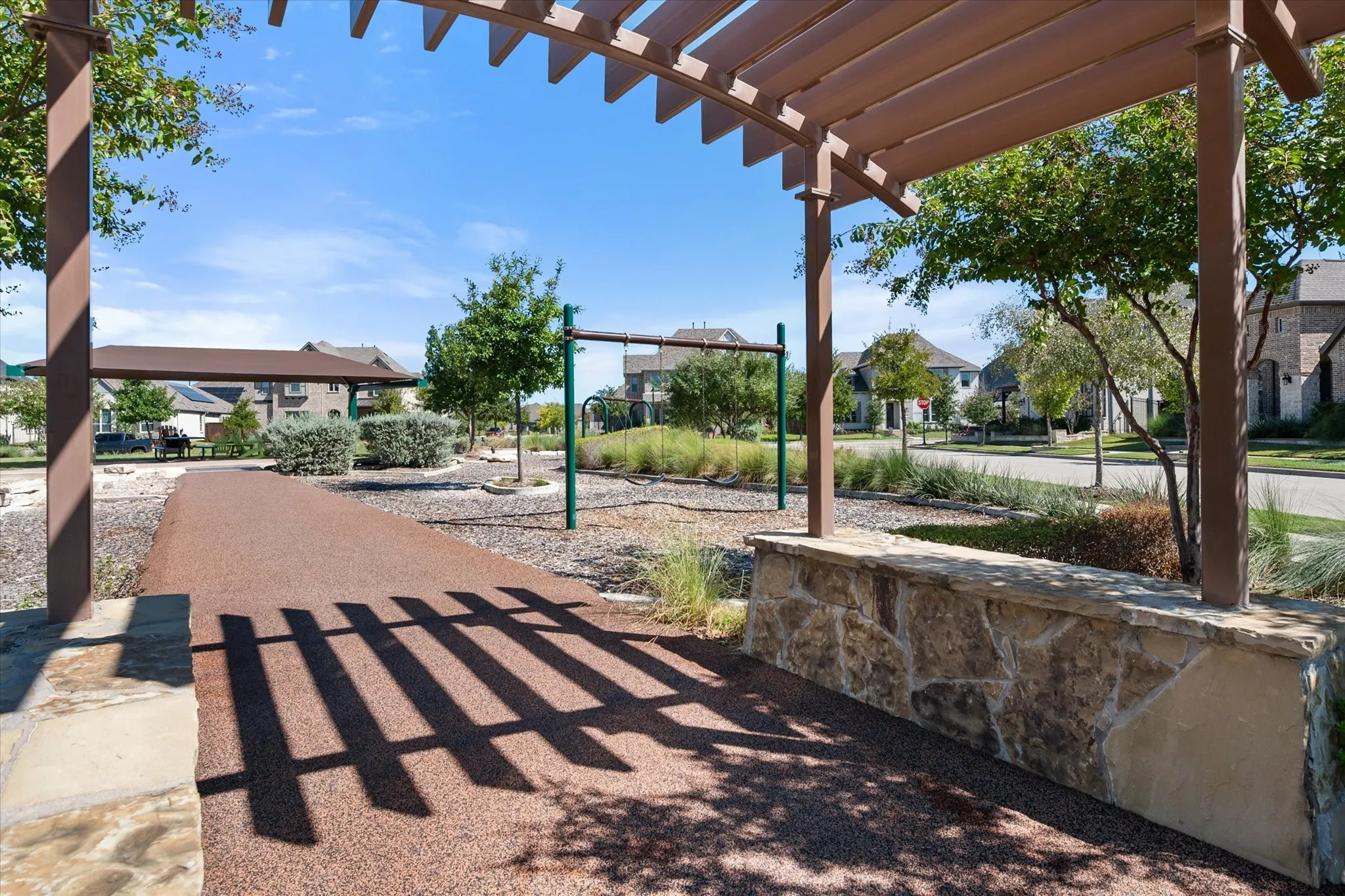 Shaded pergola structure with a stone accent wall, leading to a recreation area with a soft-surface pathway