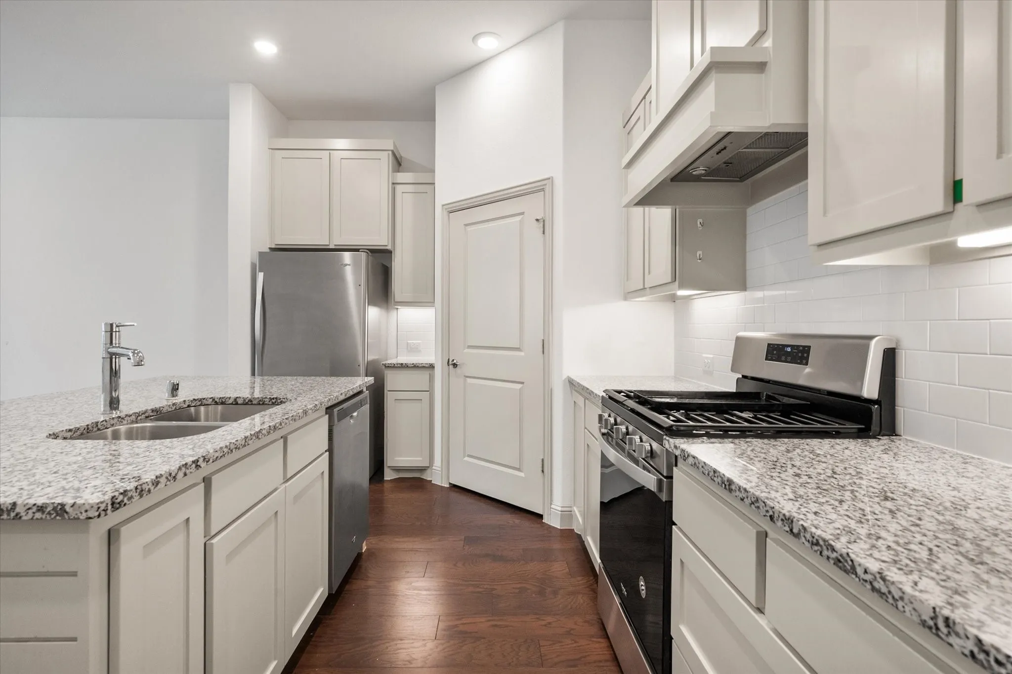 Kitchen featuring light-toned cabinetry, stainless steel appliances, granite countertops, and wood-finish flooring