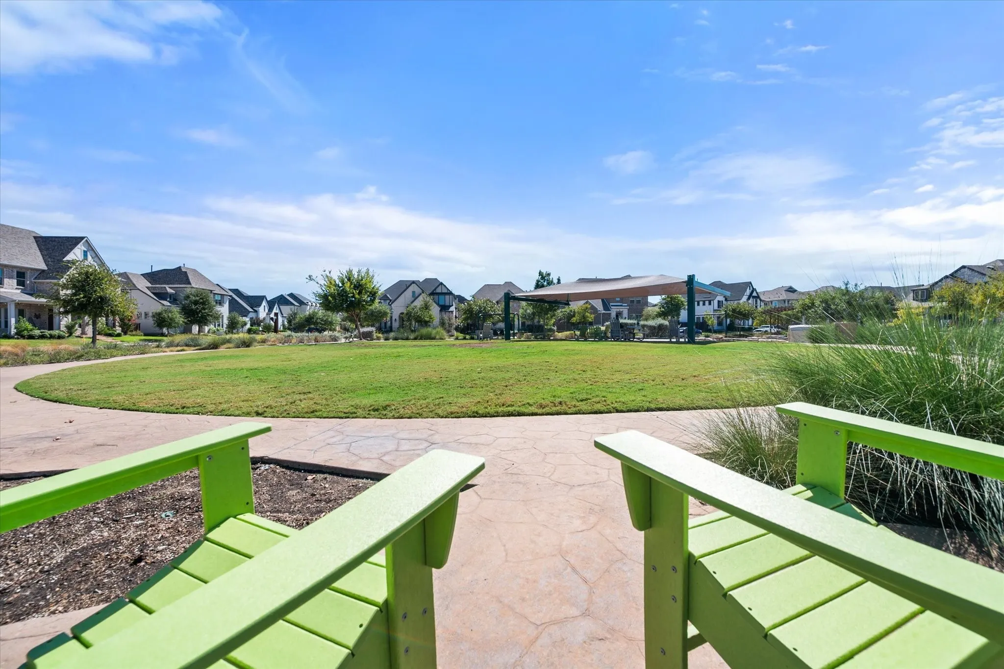 Expansive green space with walking paths, surrounding residential architecture, shaded communal area, and landscaped plantings