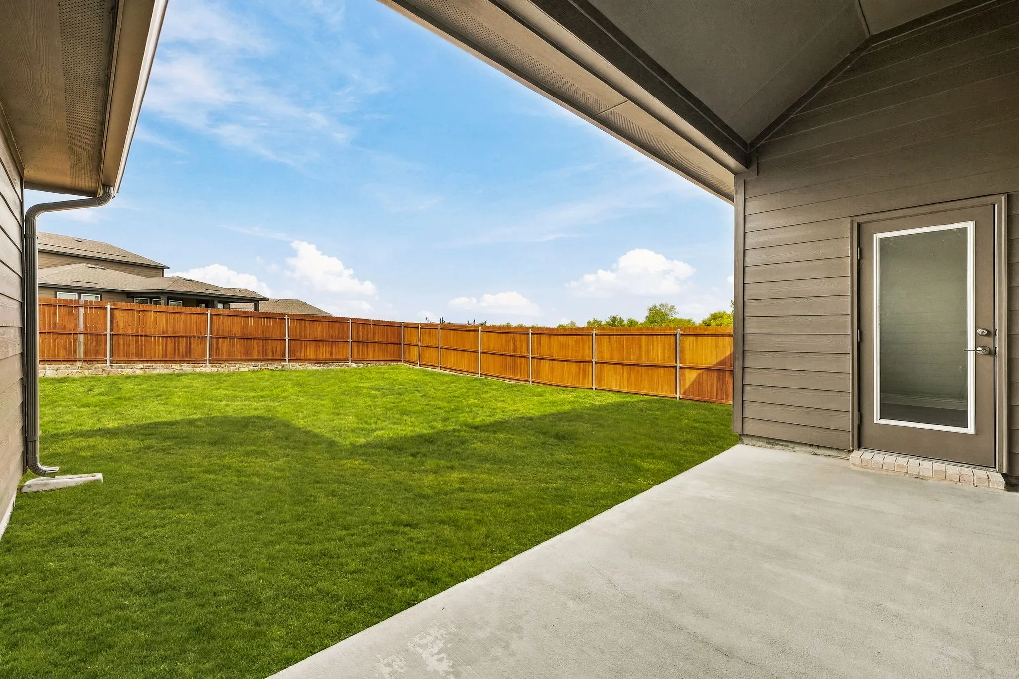 Covered concrete patio with horizontal siding exterior, expansive lawn, and wood privacy fencing
